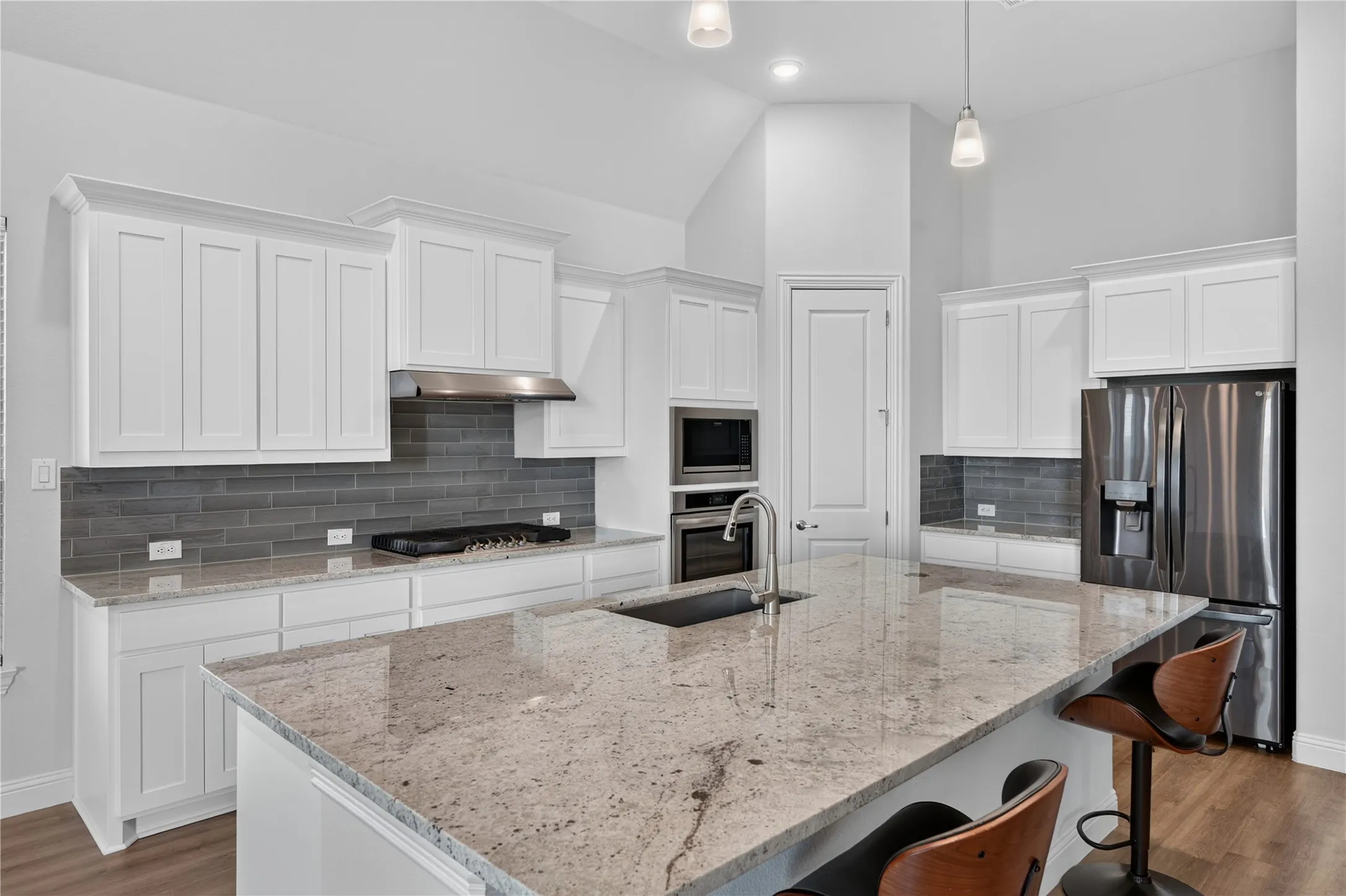 Spacious kitchen featuring white cabinetry, a large island with a composite countertop, a stainless steel gas range with a matching hood, and a stainless steel refrigerator