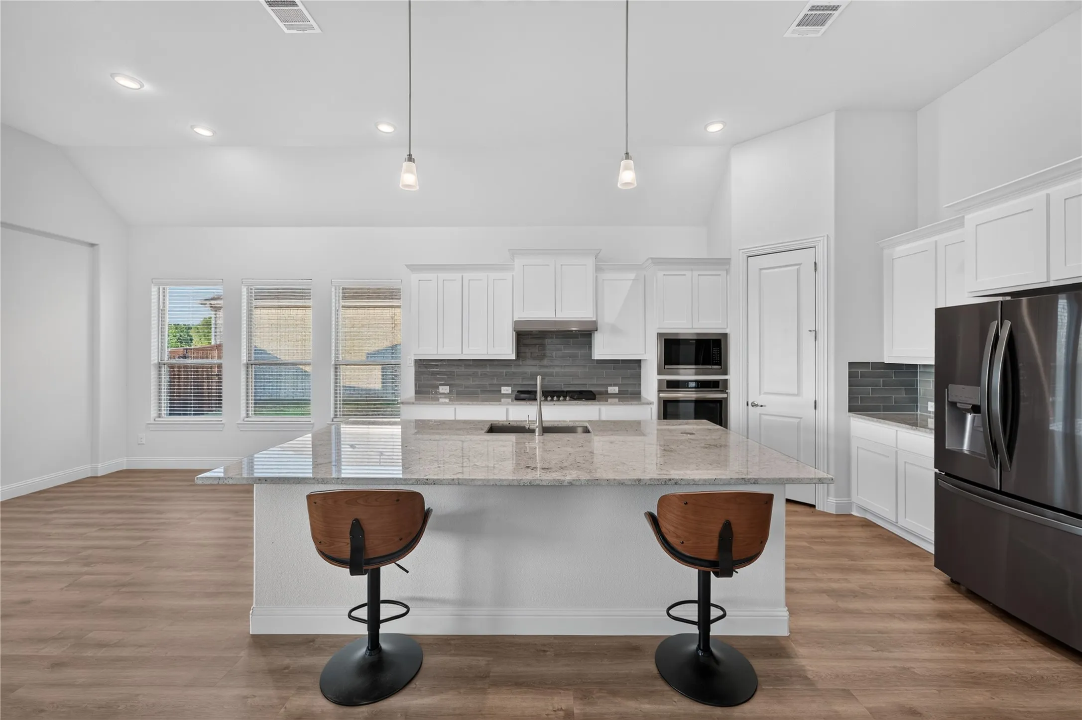 Kitchen featuring a large island with a stone countertop, white cabinetry, dark-finish appliances, and wood-finish flooring