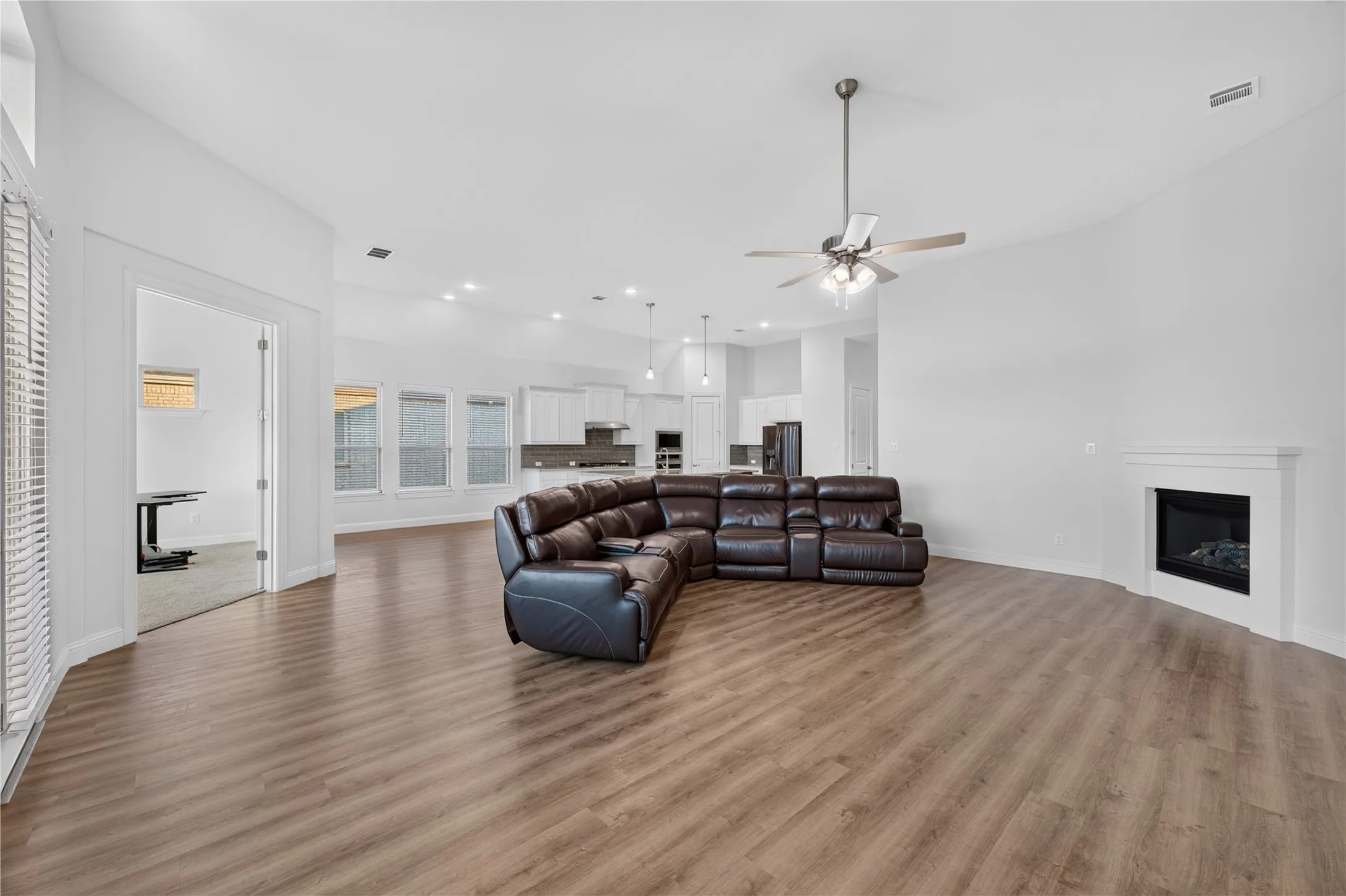 Expansive open-concept room featuring wood-finish flooring, a contemporary fireplace, and a ceiling fan