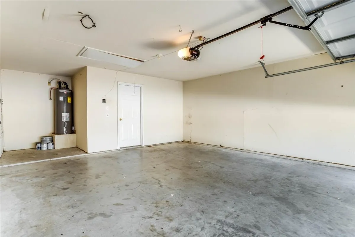 Spacious garage with concrete flooring, automatic garage door opener, interior access door, and water heater