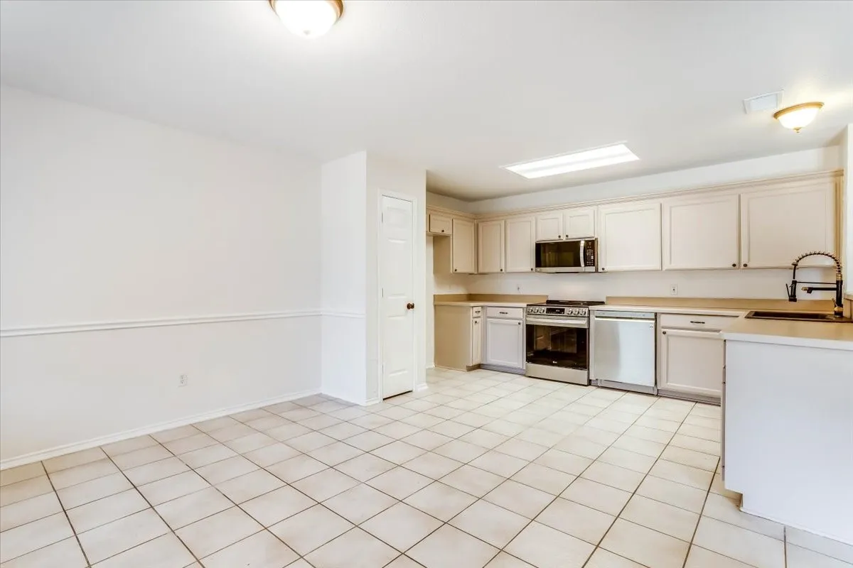 Kitchen with tile flooring, light cabinetry, stainless steel appliances, and a skylight