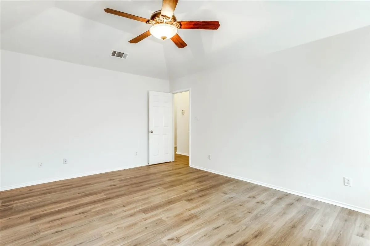 Vaulted ceiling with a ceiling fan, white paneled door, wood-finish flooring, and white baseboards