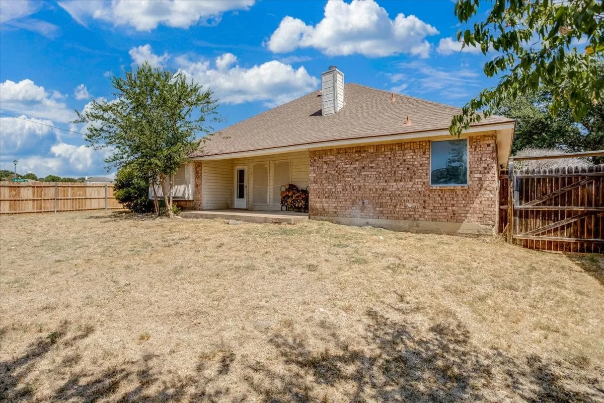 Expansive backyard featuring a privacy fence, brick exterior, and a covered patio