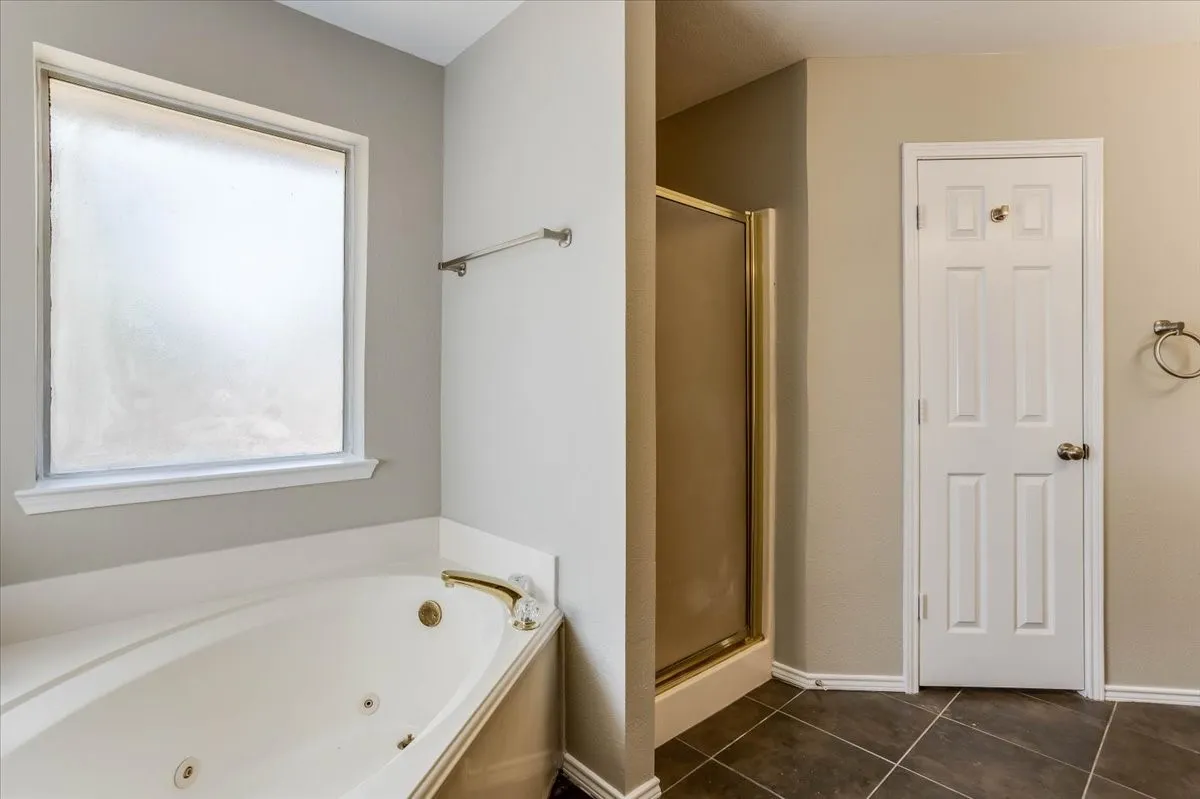 Corner soaking tub with brass fixtures, frosted window, and bronze-framed shower enclosure