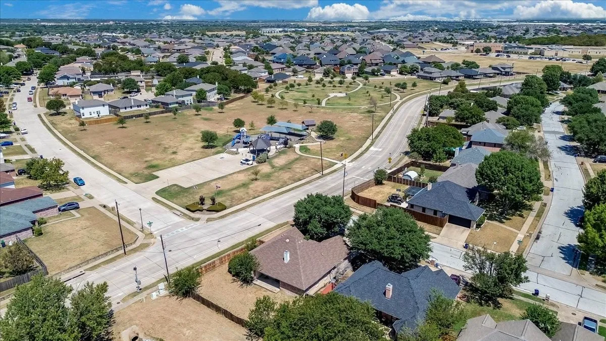 Residential neighborhood featuring mature trees, paved streets, and an open park space with playground equipment