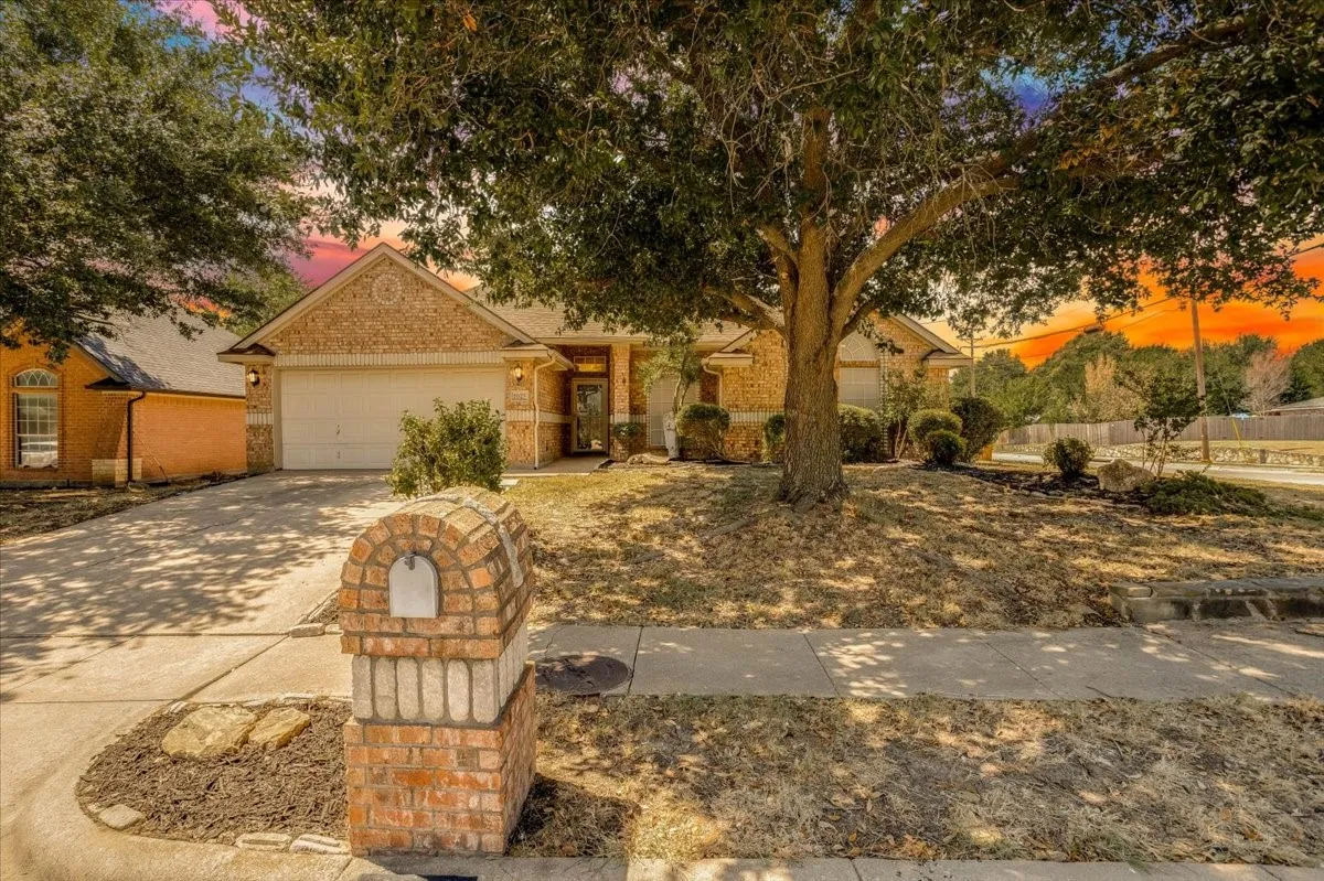 Brick and stone exterior with an attached garage, featuring a mature shade tree and a brick mailbox