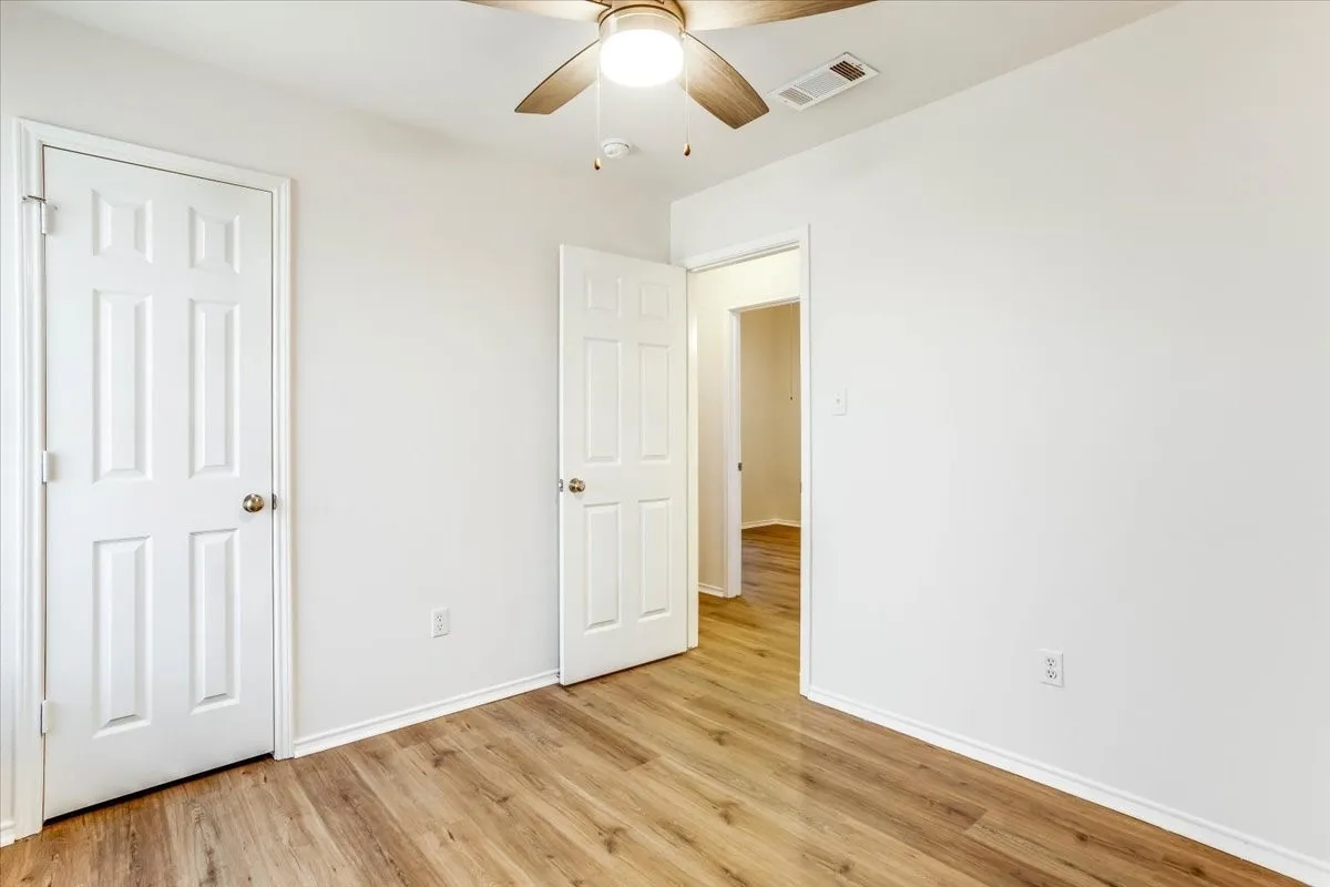 Wood-finish flooring with white baseboards, white walls, and a ceiling fan with light fixture