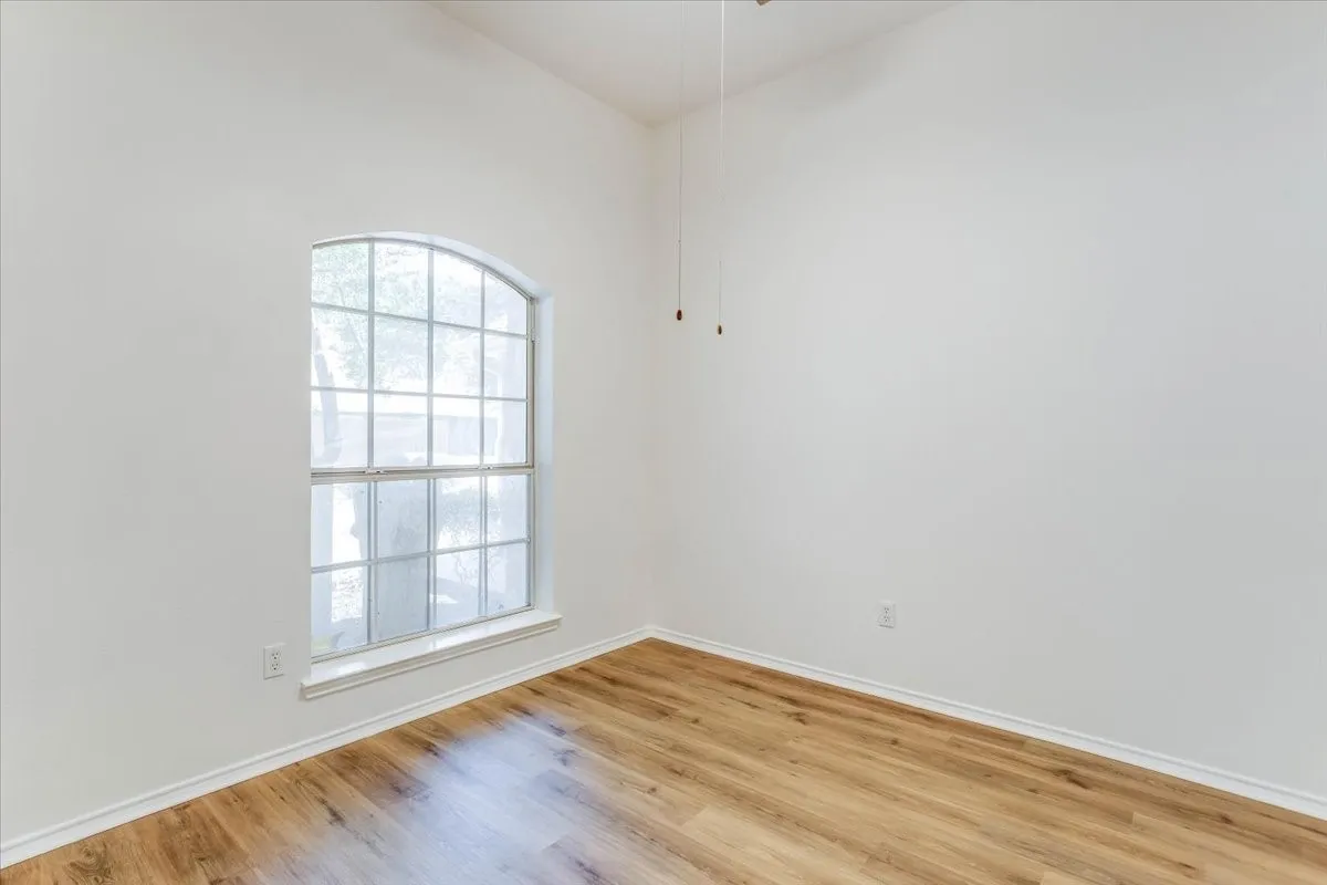 Arched window with grilles, wood-finish flooring, white walls, and a ceiling fan