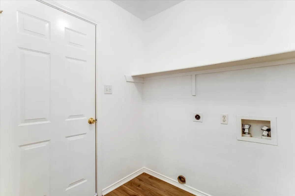 Laundry area featuring wood-finish flooring, a white paneled door, and an integrated shelf