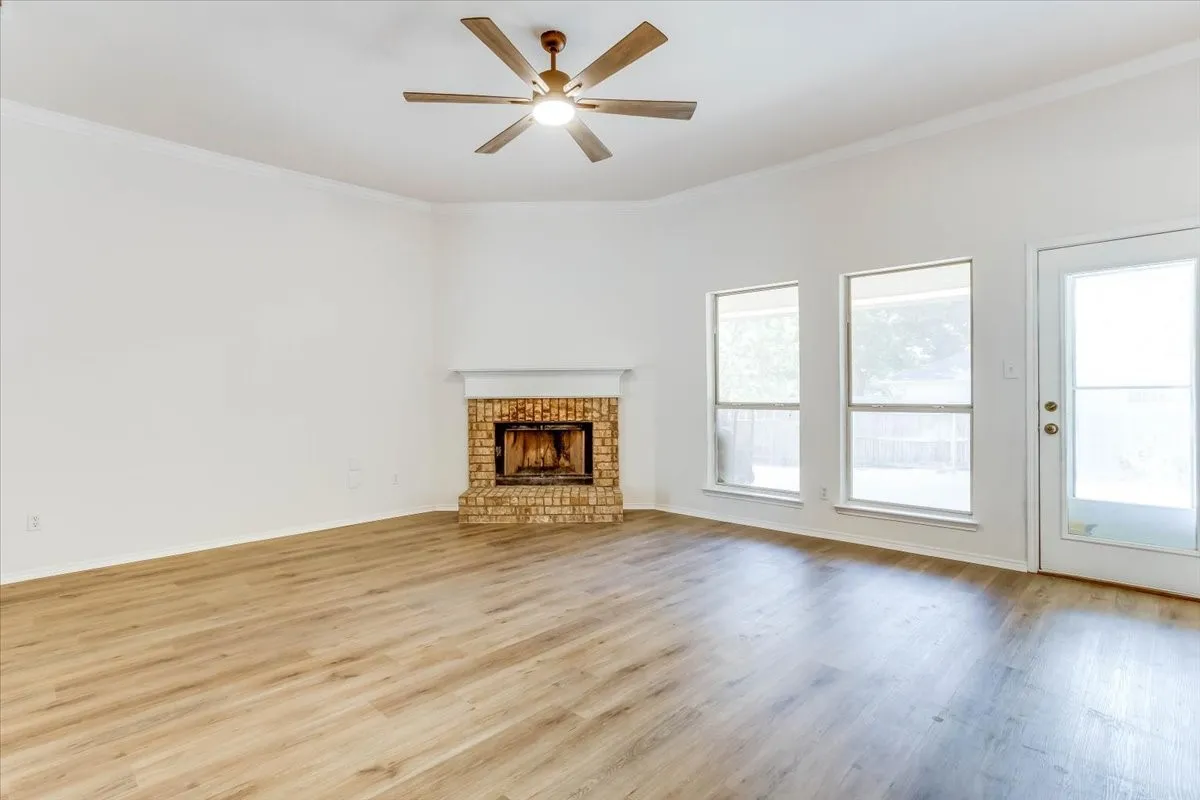 Expansive room featuring wood-finish flooring, a brick fireplace with mantel, ceiling fan, and multiple windows