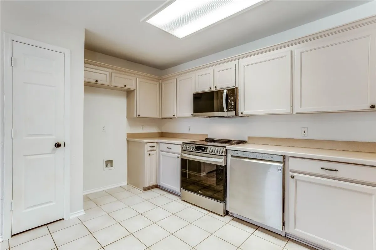 White cabinetry with dark hardware, stainless steel appliances, light-toned countertops, and white square tile flooring