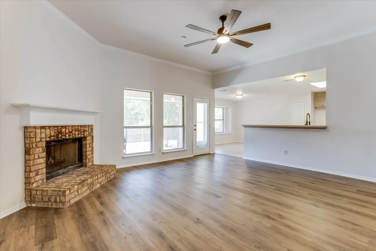Living area featuring wood-finish flooring, a brick fireplace with mantel, ceiling fan, and multiple windows
