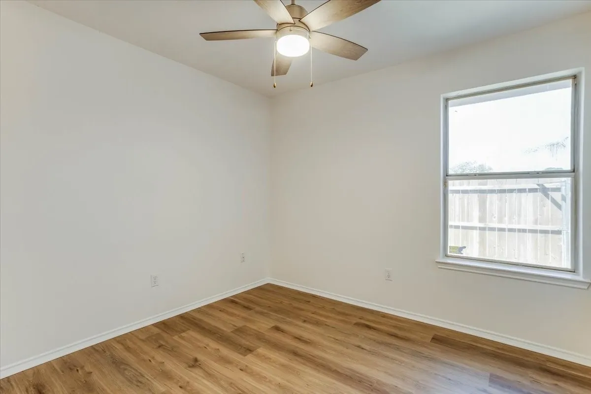 Wood-finish flooring, white walls, and a ceiling fan with integrated lighting