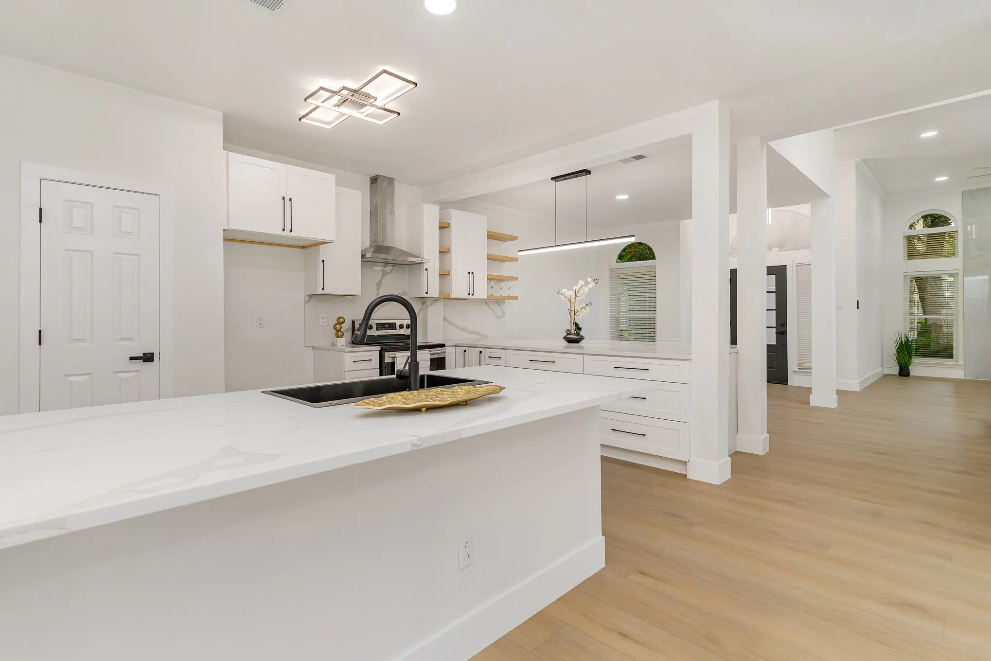Kitchen featuring hanging light fixtures, wall chimney range hood, light stone countertops, white cabinetry, and light hardwood / wood-style flooring