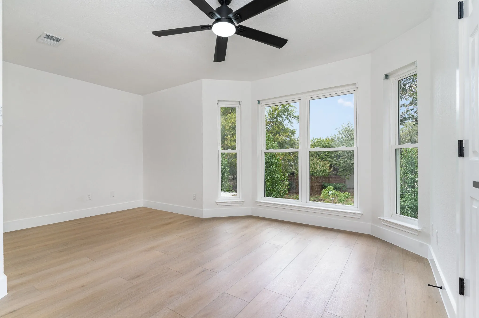 Empty room with a wealth of natural light, light hardwood / wood-style floors, and ceiling fan