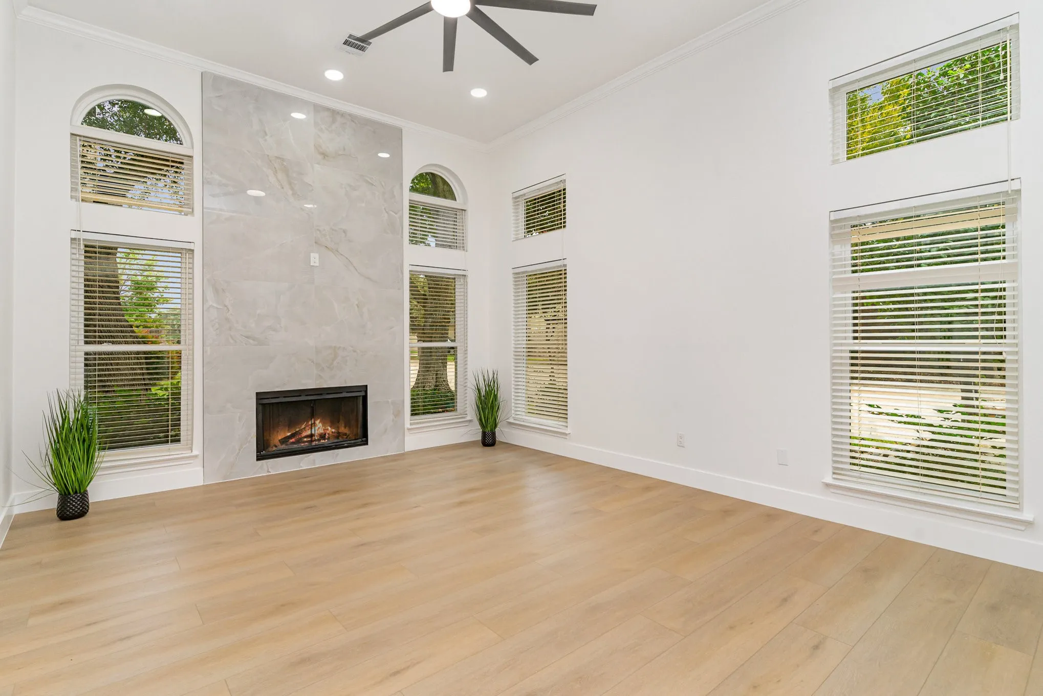 Unfurnished living room with ornamental molding, ceiling fan, a premium fireplace, a towering ceiling, and light wood-type flooring