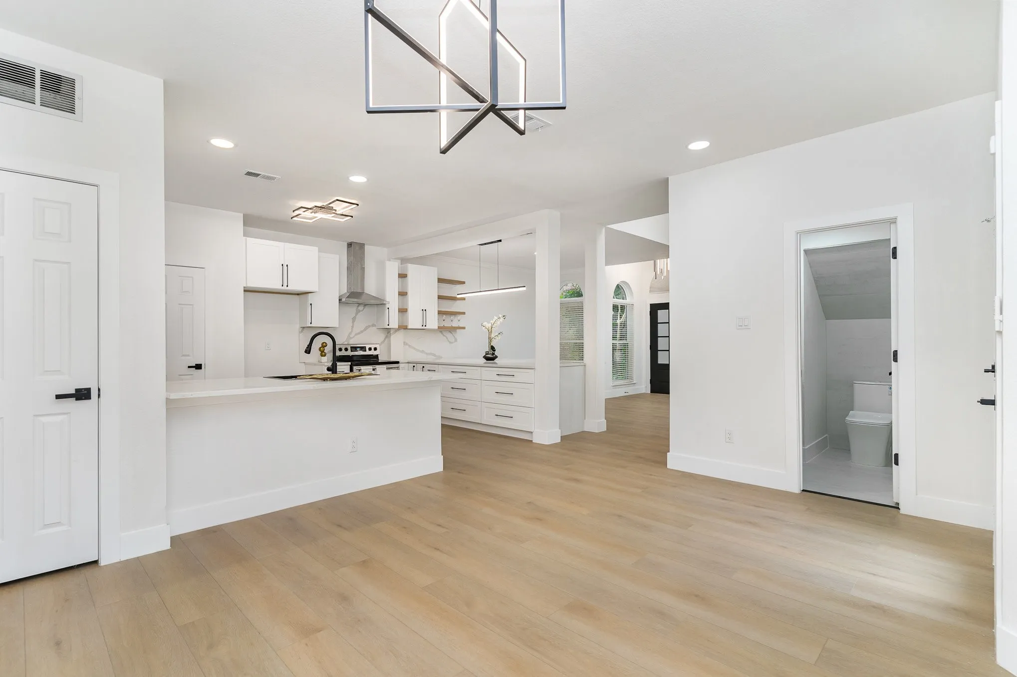Kitchen featuring light wood-type flooring, white cabinetry, kitchen peninsula, and wall chimney range hood