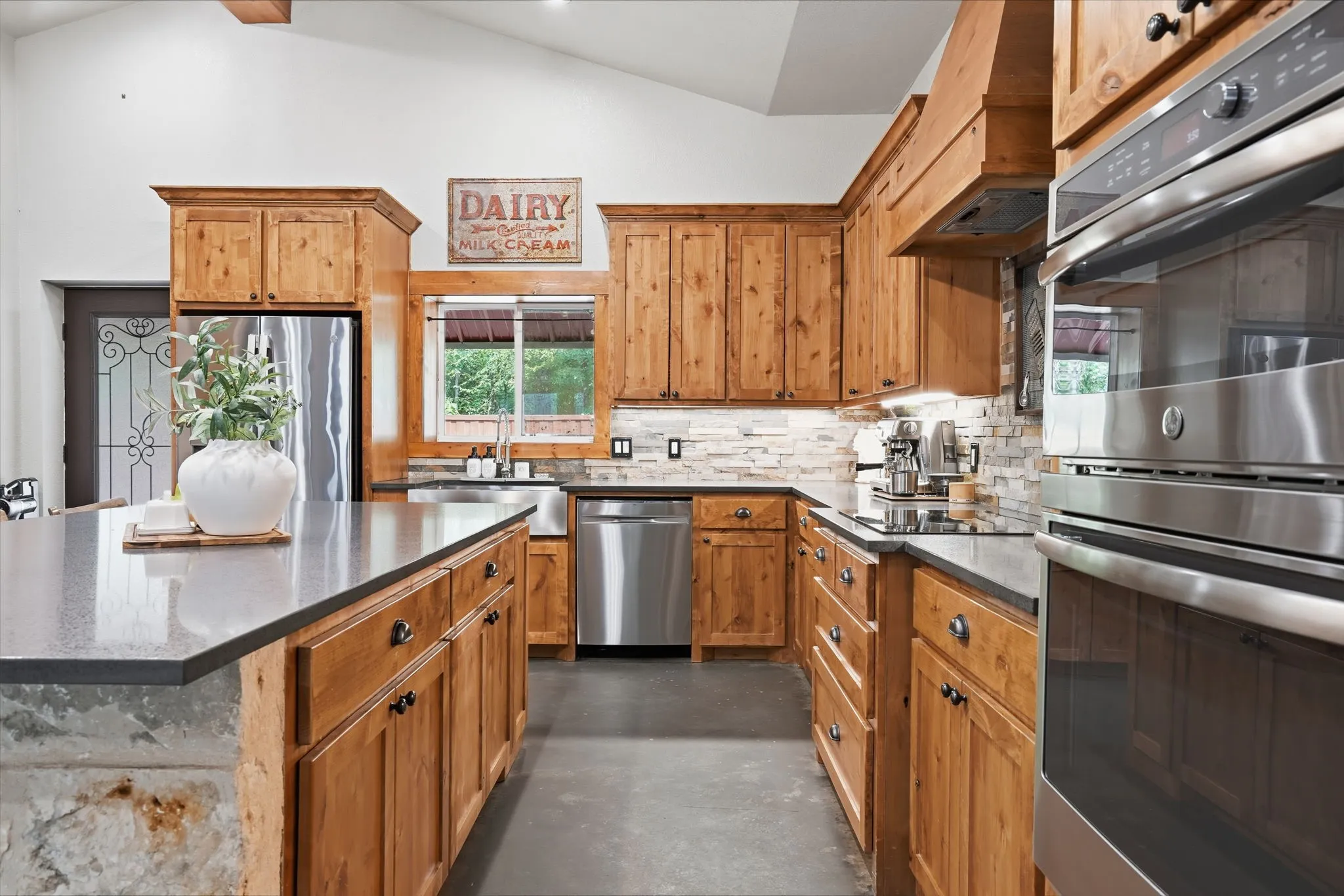 Kitchen featuring wood cabinetry, stainless steel appliances, dark countertops, and a stone-clad kitchen island