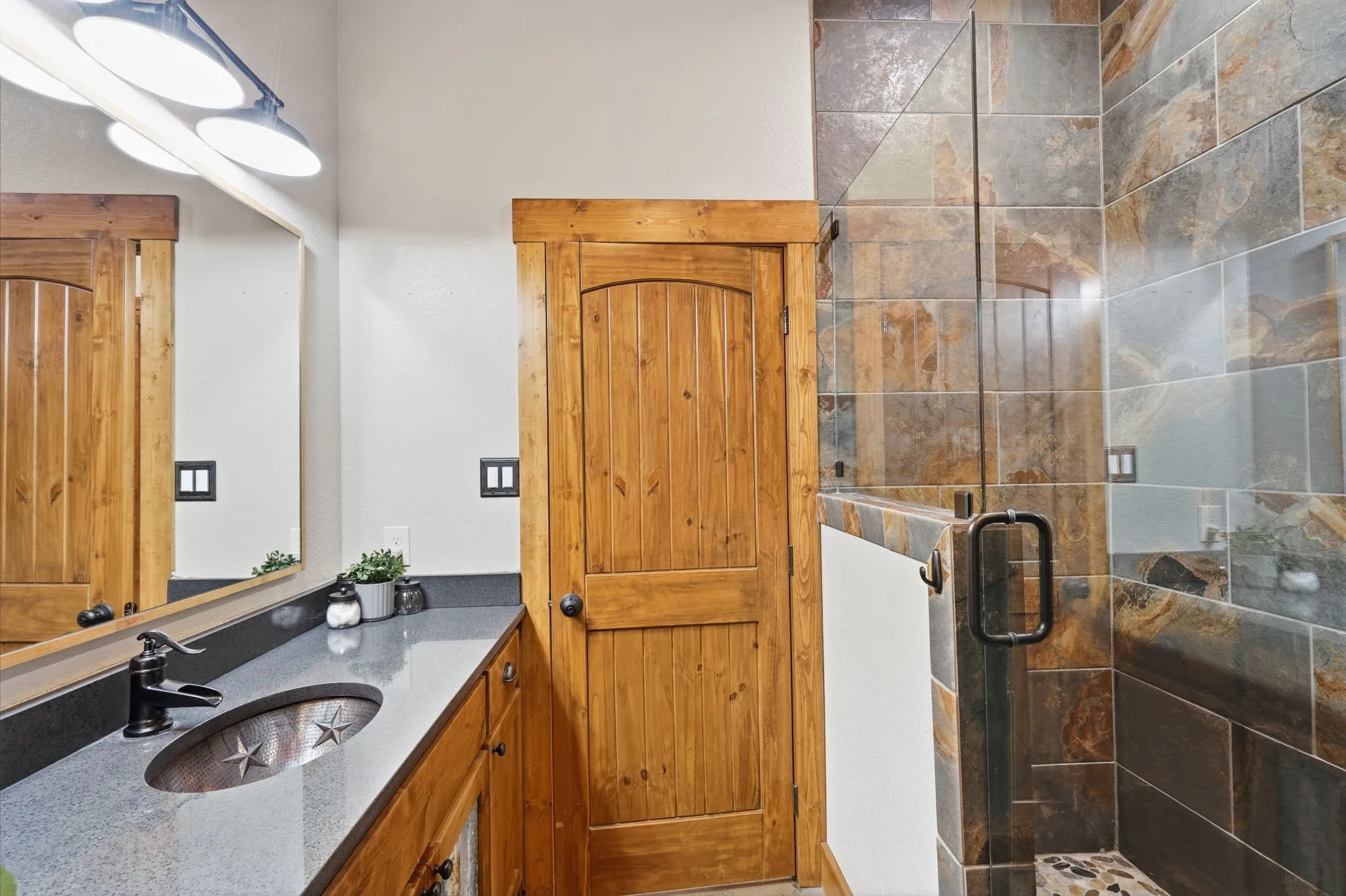 Custom vanity with a metallic vessel sink and dark countertop, complemented by a wood-finish door and wood-framed mirror