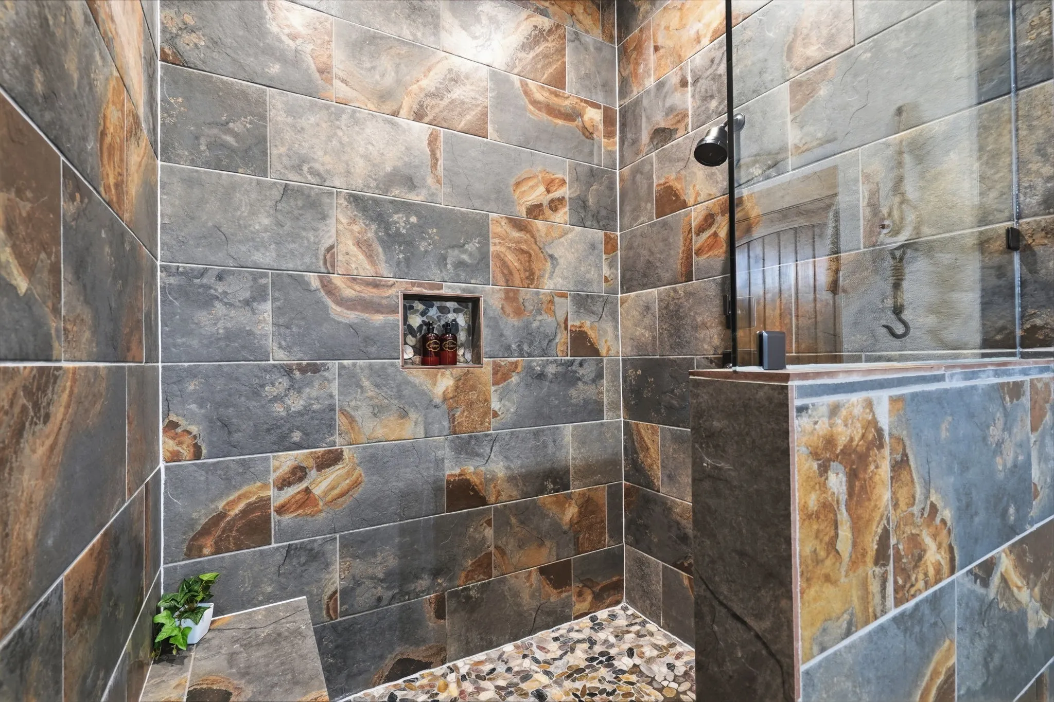 Walk-in shower with natural stone tile walls, a built-in shower niche, and a glass partition
