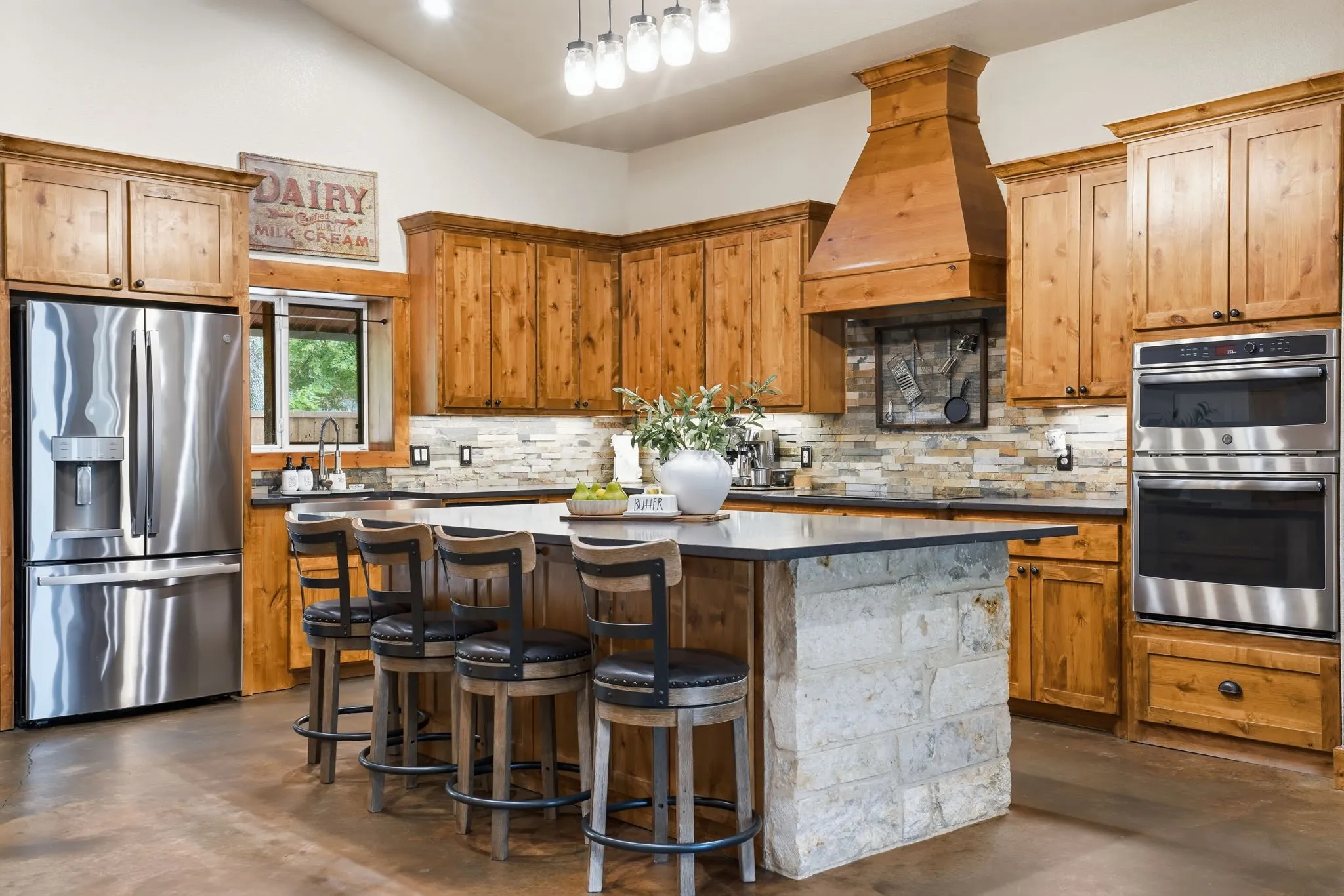 Kitchen featuring custom wood cabinetry, stainless steel appliances, a stone-clad island, a tile backsplash, and wood-finish flooring