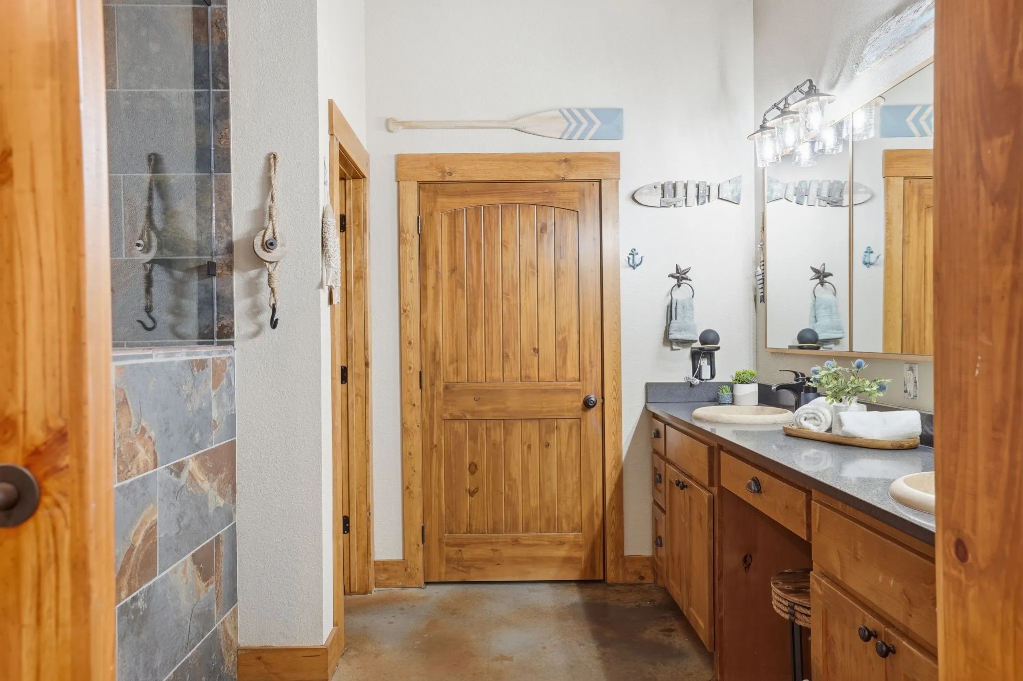 Wood-finish shaker cabinetry, dual vessel sinks, and a dark stone-finish countertop