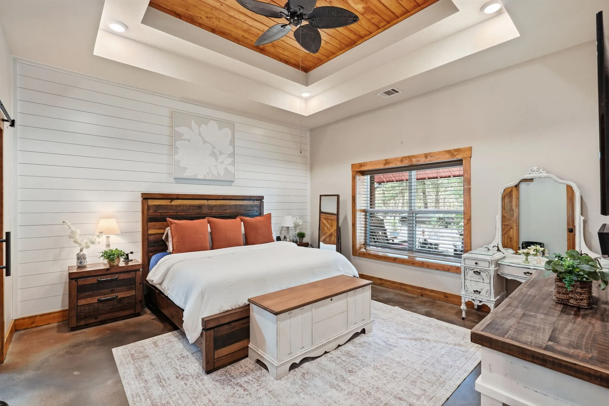 Tray ceiling with wood-finish inlay and ceiling fan, shiplap accent wall, wood-trimmed window, concrete flooring, and barn door entry