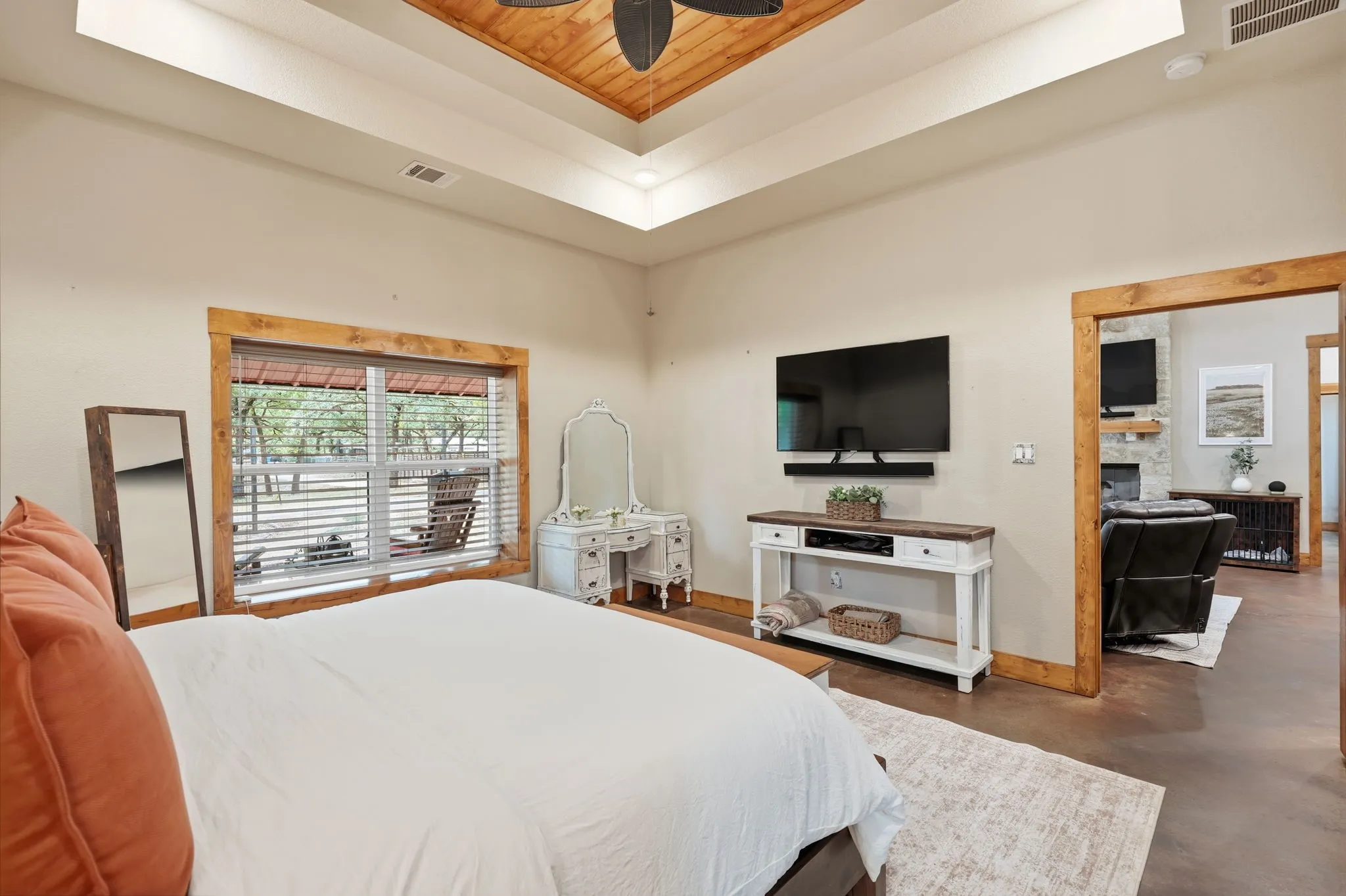 Tray ceiling with wood-finish paneling, an expansive window with wooden trim, and an open doorway featuring wooden casing