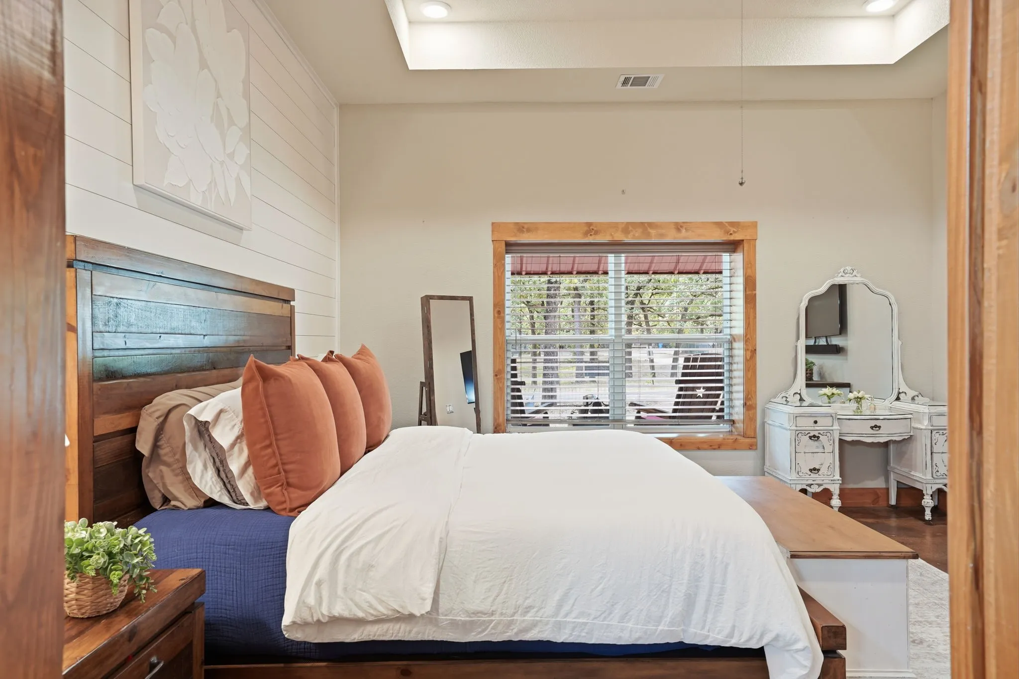Wood-finish flooring, shiplap accent wall, tray ceiling with recessed lighting, and a window with wood trim