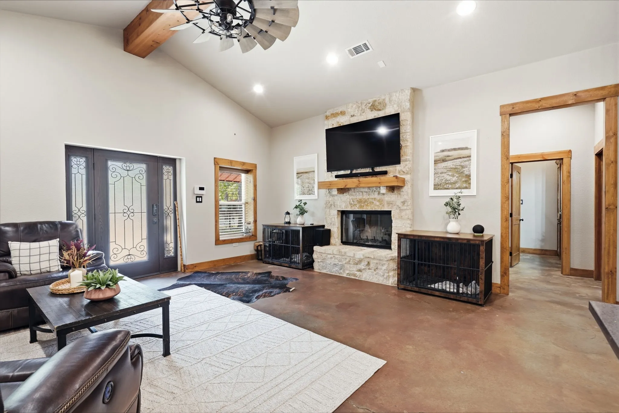Vaulted ceiling with exposed wood beam, stone fireplace with wood mantel, sealed concrete flooring, wood window trim, and wood door frames