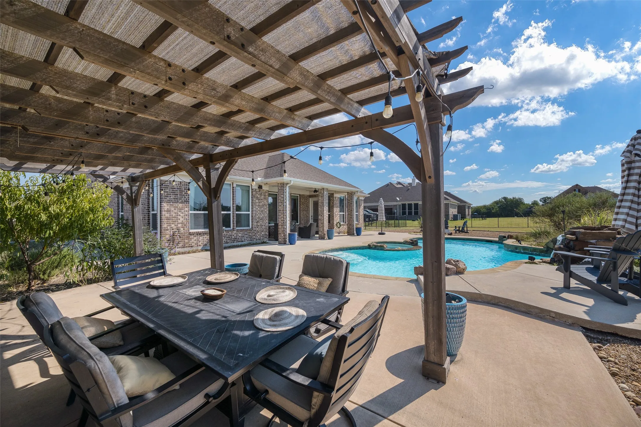 Expansive outdoor living area featuring a wooden pergola, concrete patio, and a built-in swimming pool with an integrated spa
