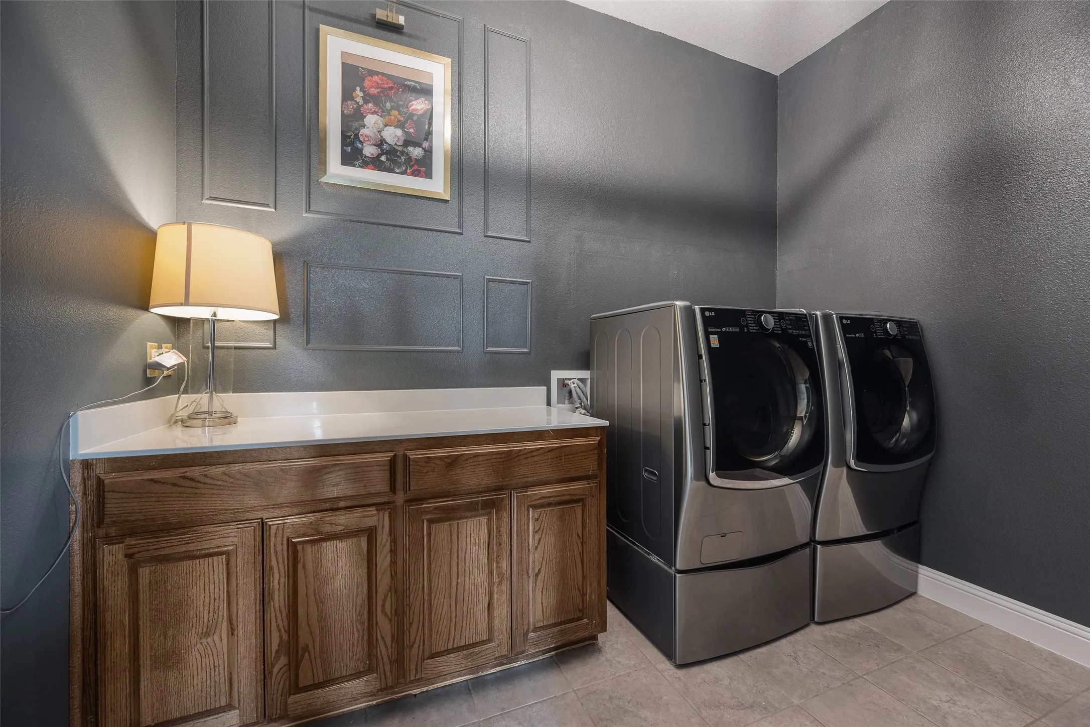 Wood-finish cabinetry with a light-toned countertop, textured wall paneling, and ceramic tile flooring