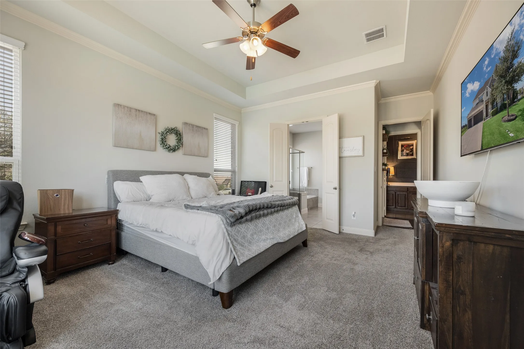 Tray ceiling with crown molding, ceiling fan with light fixture, carpeted flooring, and two windows with blinds