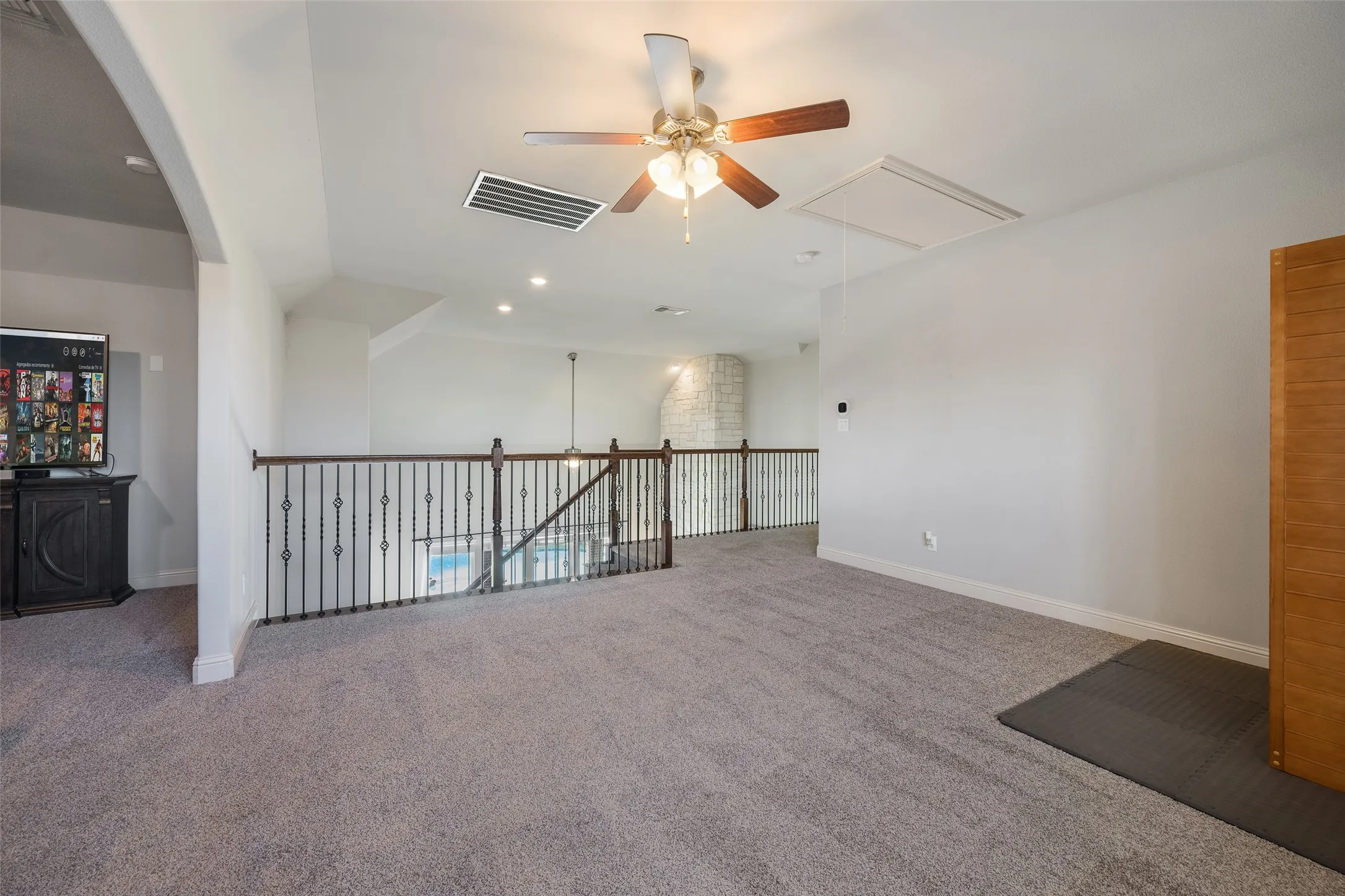 Carpeted loft area featuring a ceiling fan with integrated lighting, recessed lighting, and an ornate wrought iron railing