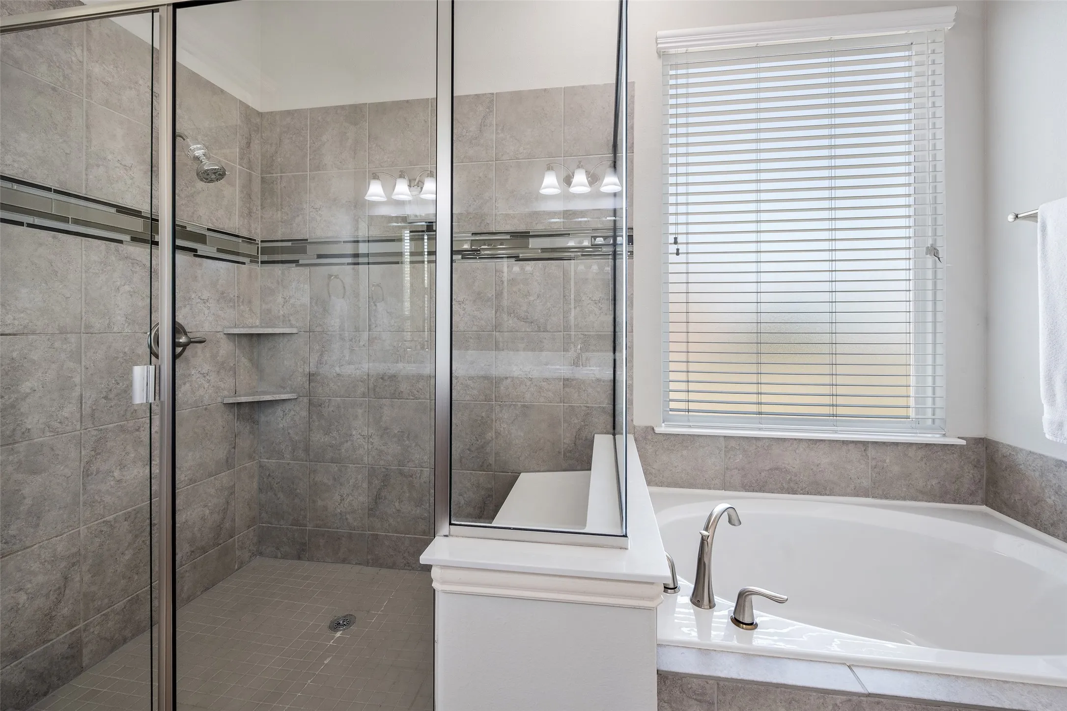 Glass-enclosed shower with tile surround and built-in shelving, accompanied by a separate soaking tub with deck-mounted fixtures