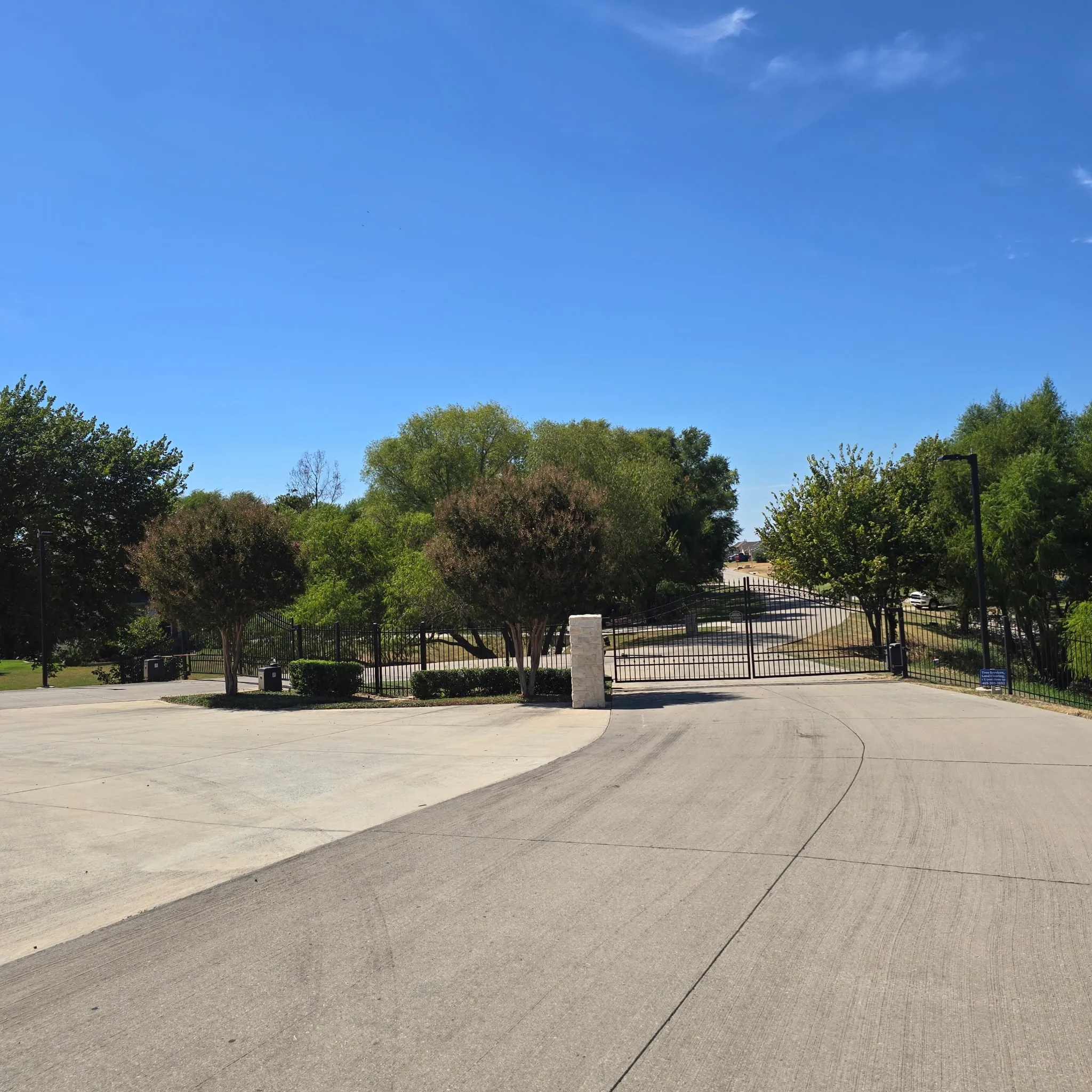 Gated community entrance with mature trees and paved roadways