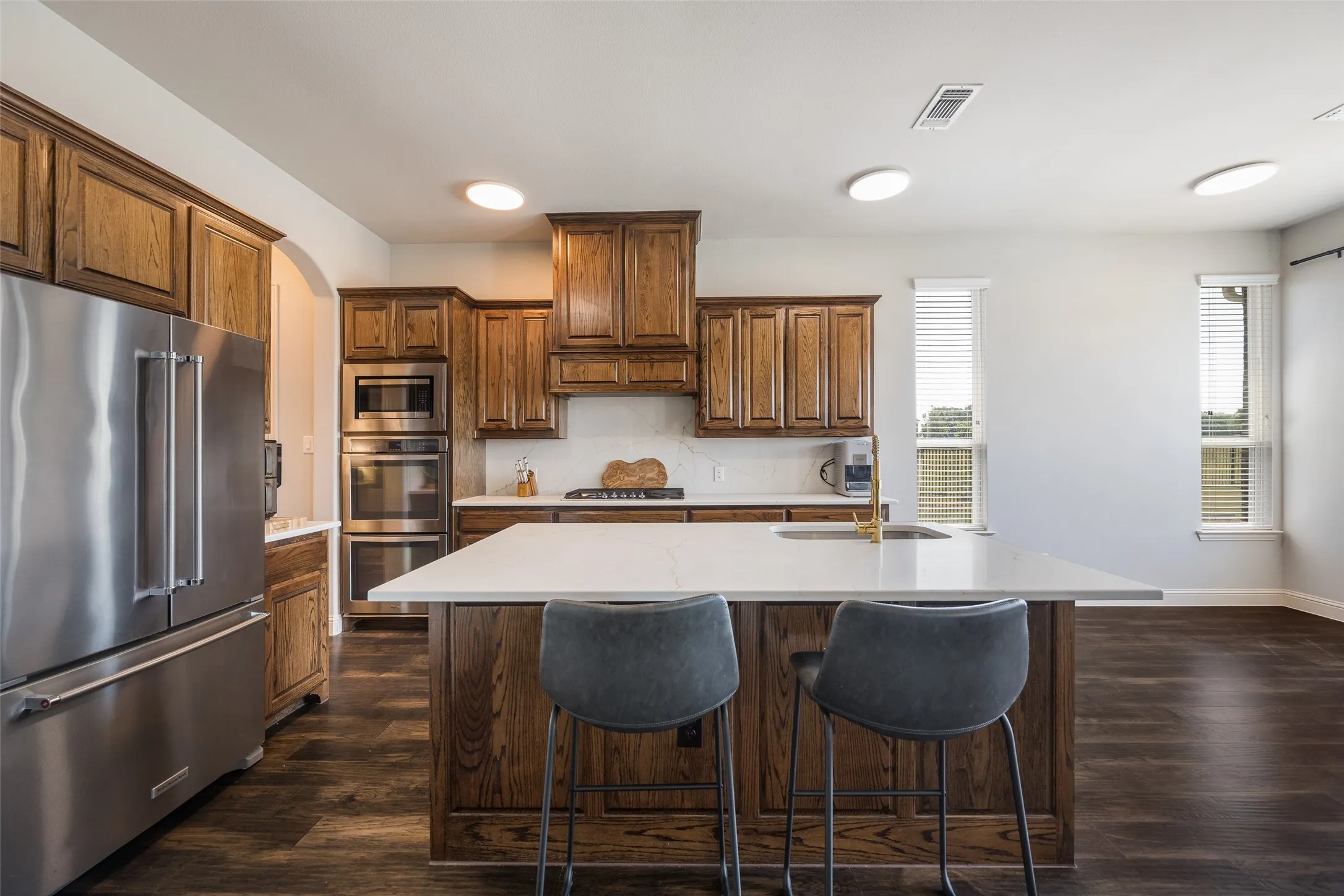 Contemporary kitchen featuring custom wood cabinetry, stainless steel appliances including dual wall ovens, quartz countertops, and a generously proportioned island with seating for two