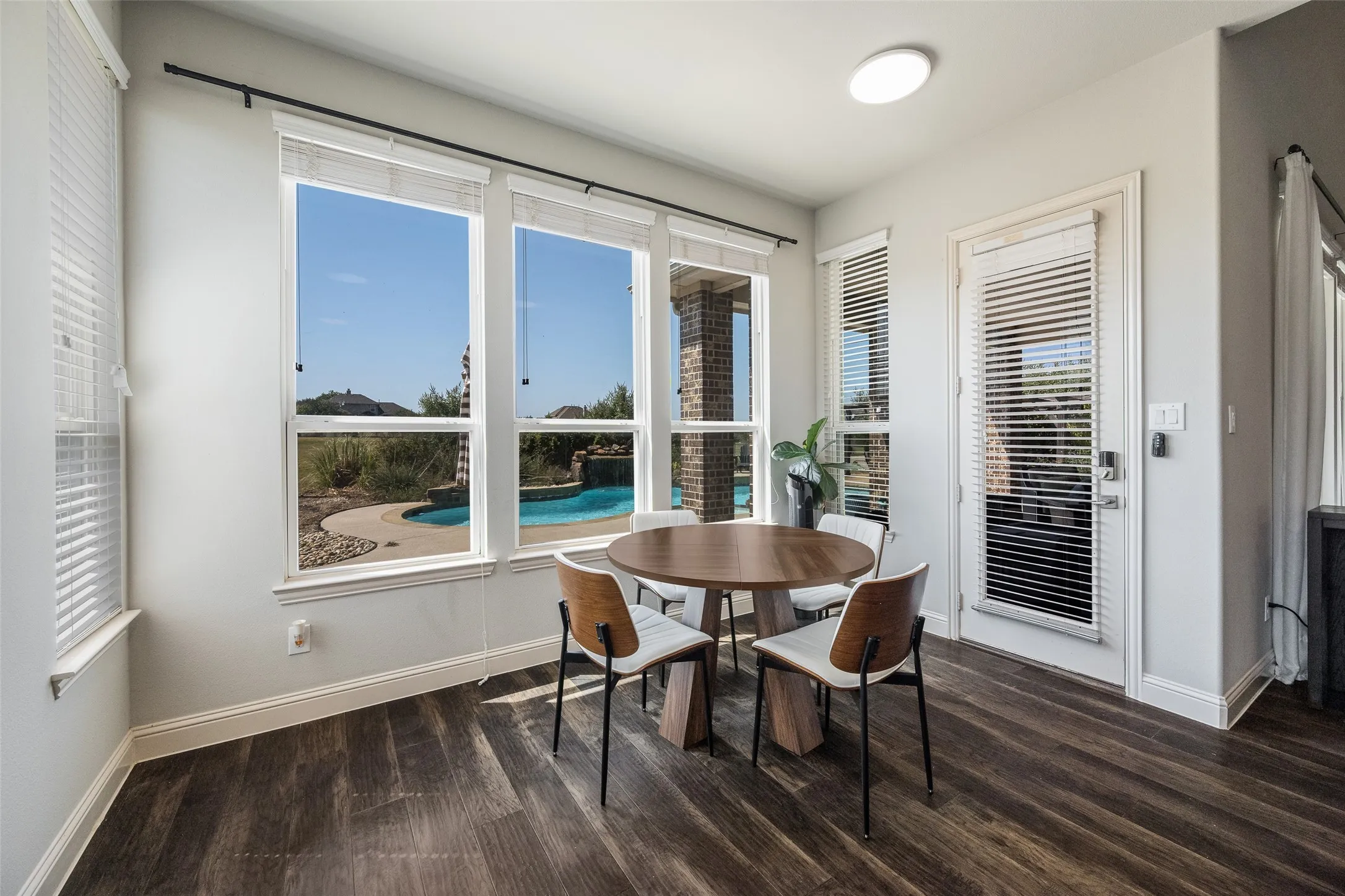 Bright sunroom with expansive glass doors and windows framing pool and landscape vistas, wood-finish flooring, recessed ceiling lighting, and direct access to outdoor living spaces