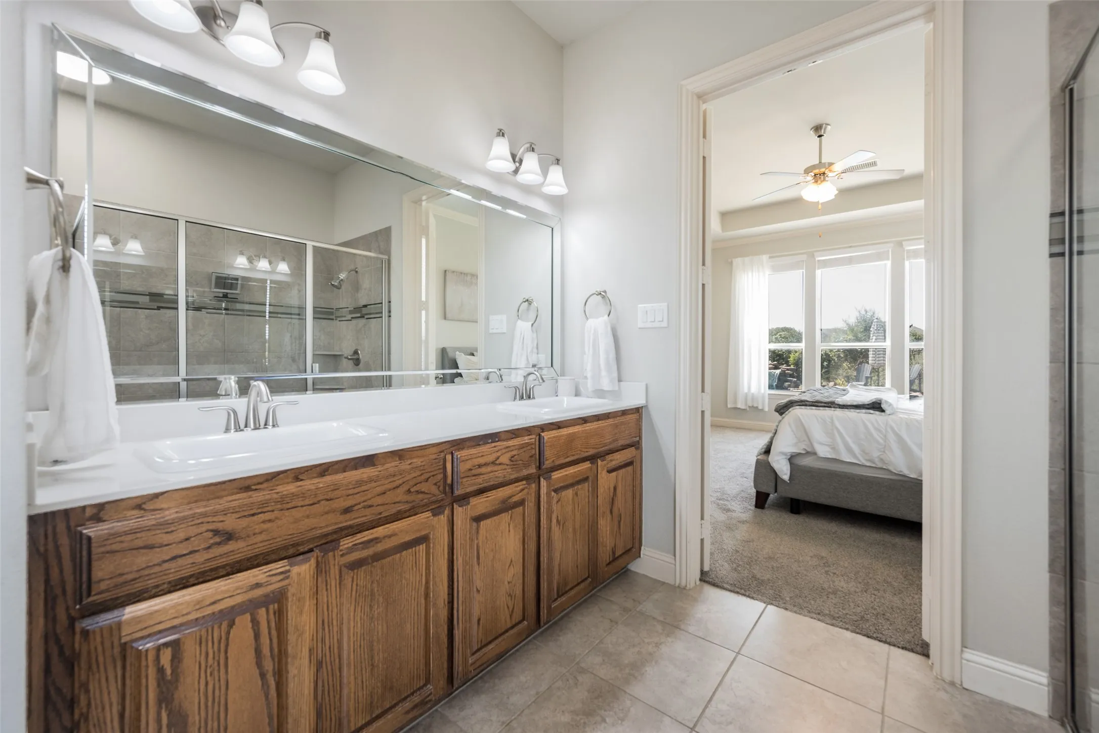 Primary bathroom featuring an extensive wood-finish vanity with dual sinks, white quartz countertop, and polished nickel fixtures