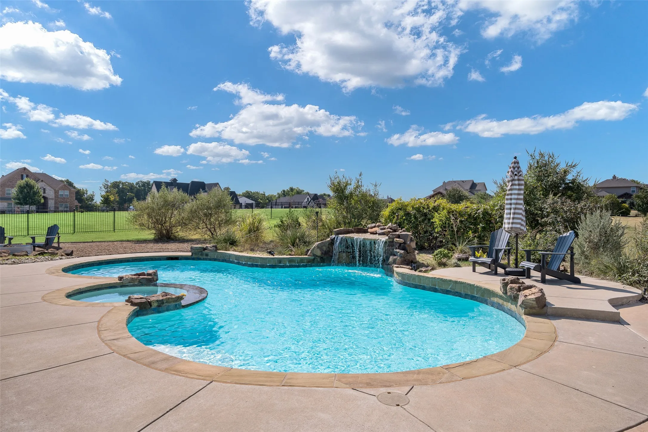 Custom-shaped swimming pool with an integrated spa, rock-feature waterfall, and ample concrete decking