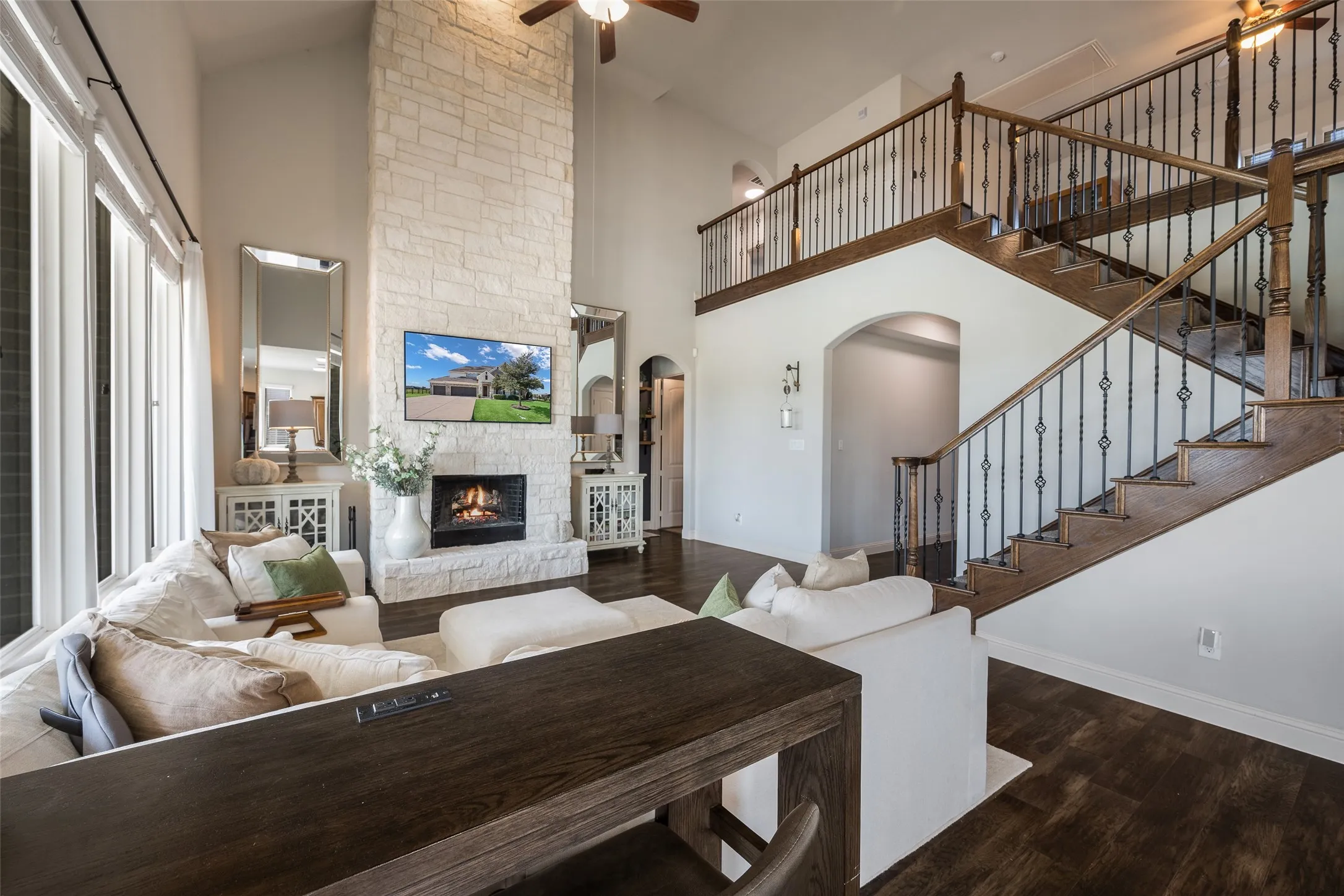 Two-story living area with a stone fireplace, wood-finish flooring, and a grand staircase with wrought iron balusters