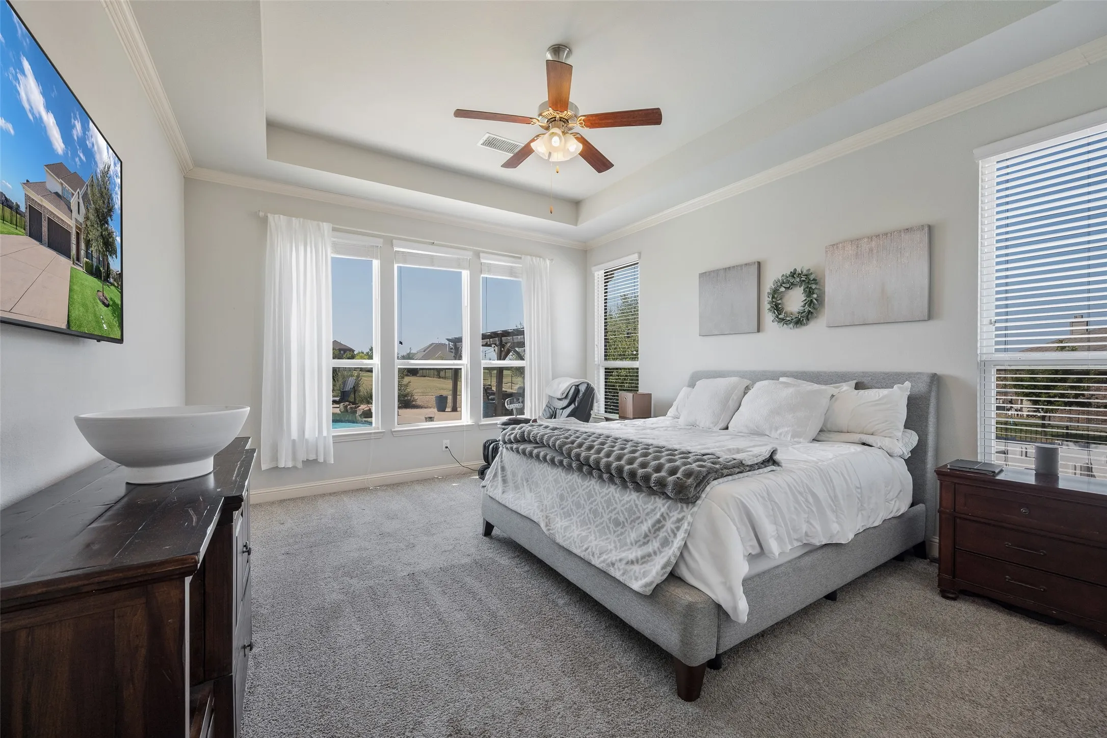 Tray ceiling with crown molding, ceiling fan with wood-finish blades, large windows, and wall-to-wall carpeting