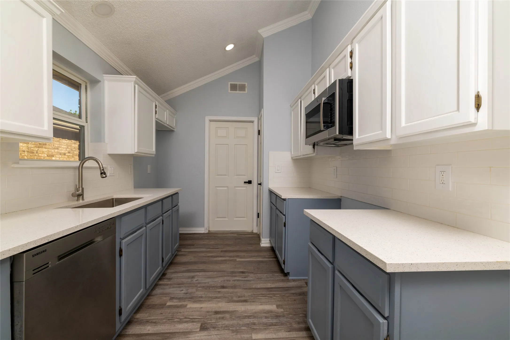 Kitchen featuring vaulted ceilings, wood-finish flooring, white shaker-style upper cabinetry, blue shaker-style lower cabinetry, and light-toned countertops