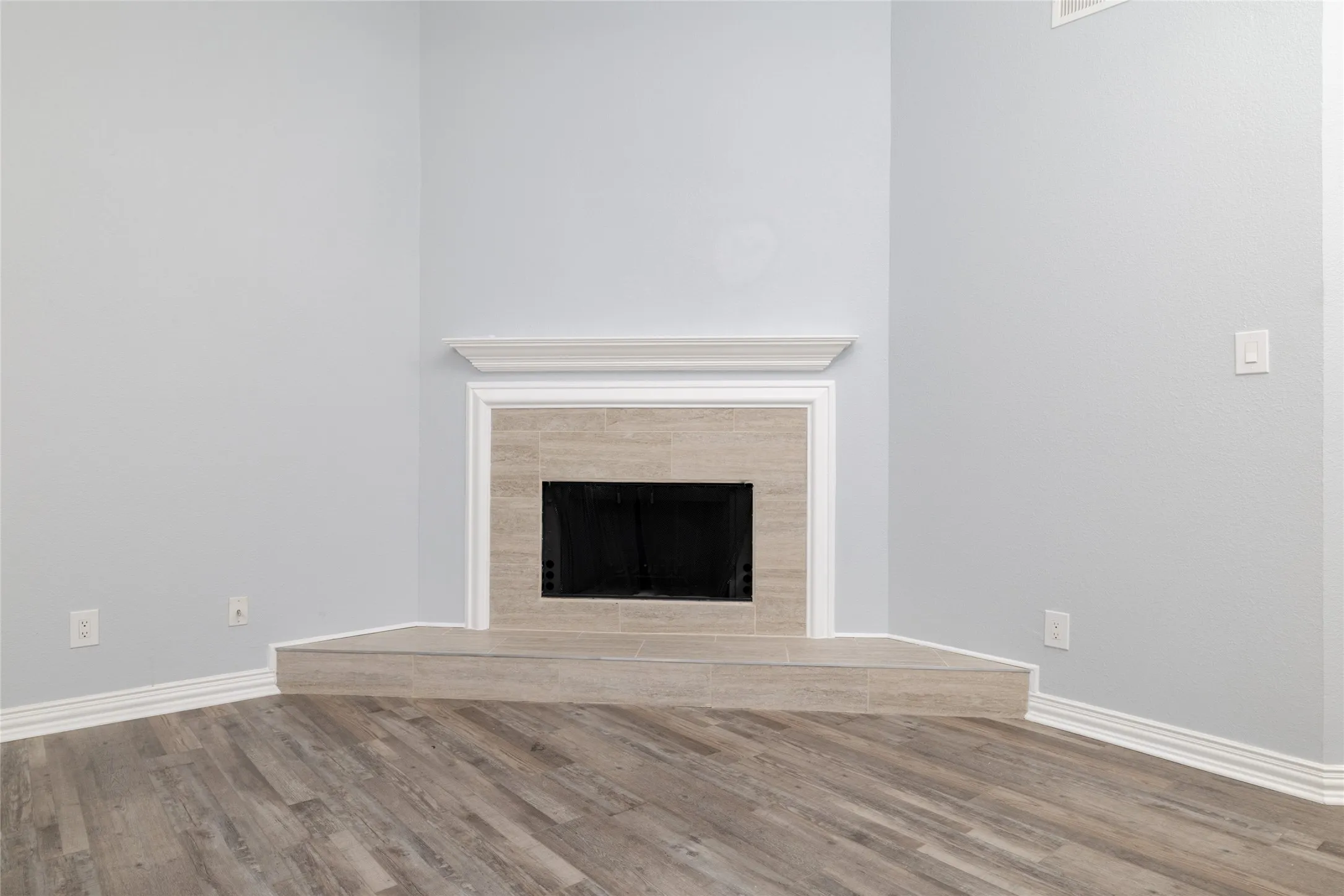 Corner fireplace featuring a tile surround and hearth, crown molding, and wood-like LVP flooring