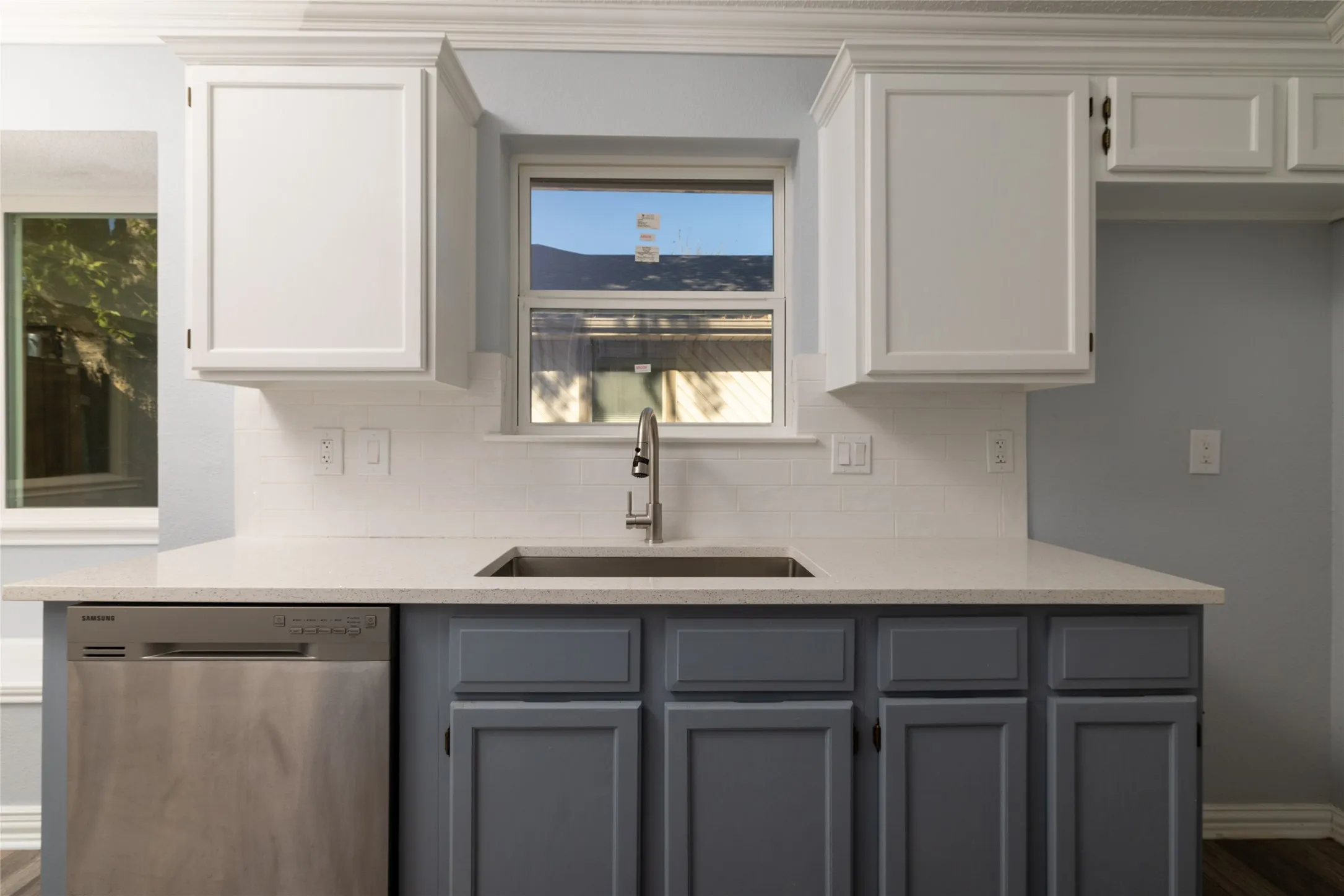 Dual-toned cabinetry, stainless steel dishwasher, undermount sink with a chrome faucet, light-toned countertop, and white subway tile backsplash