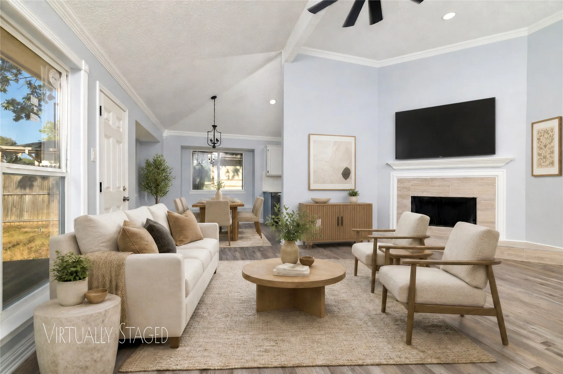 Vaulted ceiling with exposed beams, wood-finish flooring, fireplace with stone surround, crown molding, and a ceiling fan