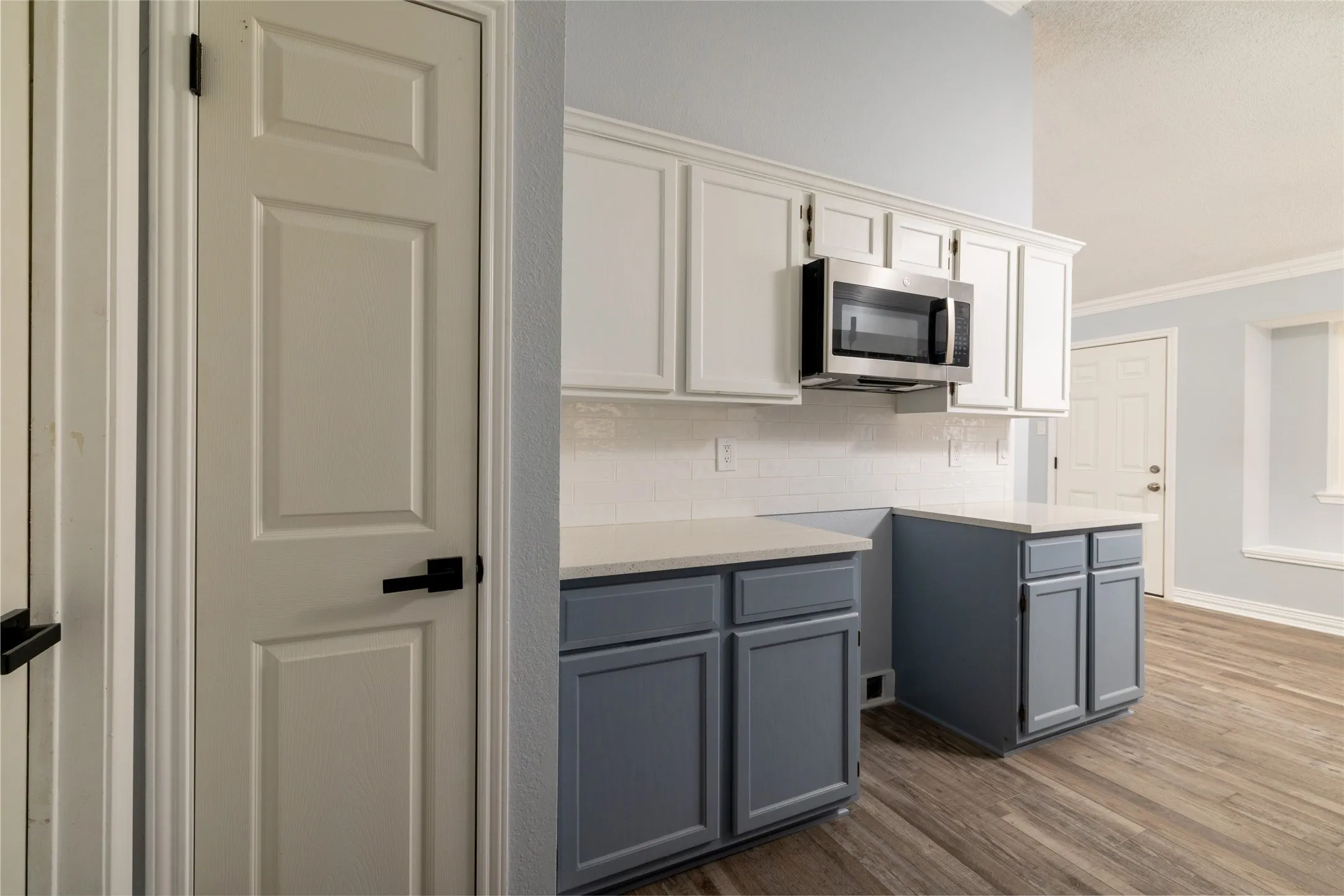 Kitchen featuring wood-like LVP  flooring, two-tone cabinetry with white upper and grey lower units, stainless steel microwave, white subway tile backsplash, and light-toned countertops
