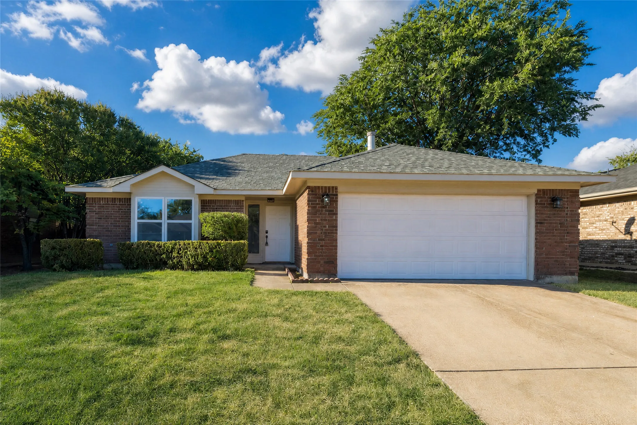Brick exterior with an attached garage, paved driveway, and a front bay window