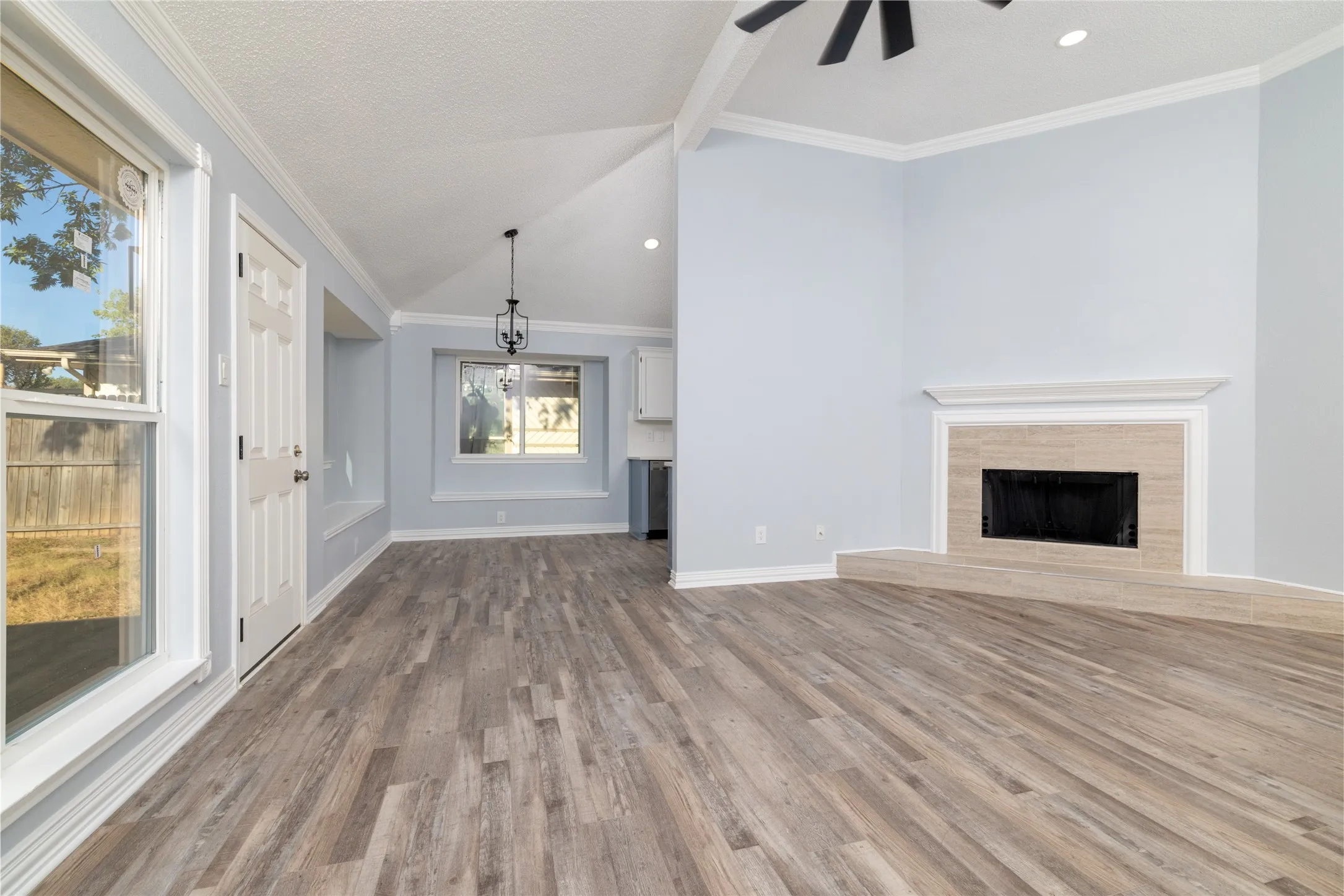 Vaulted ceiling with exposed beam, wood-finish flooring, fireplace with tiled surround, ceiling fan, and recessed lighting