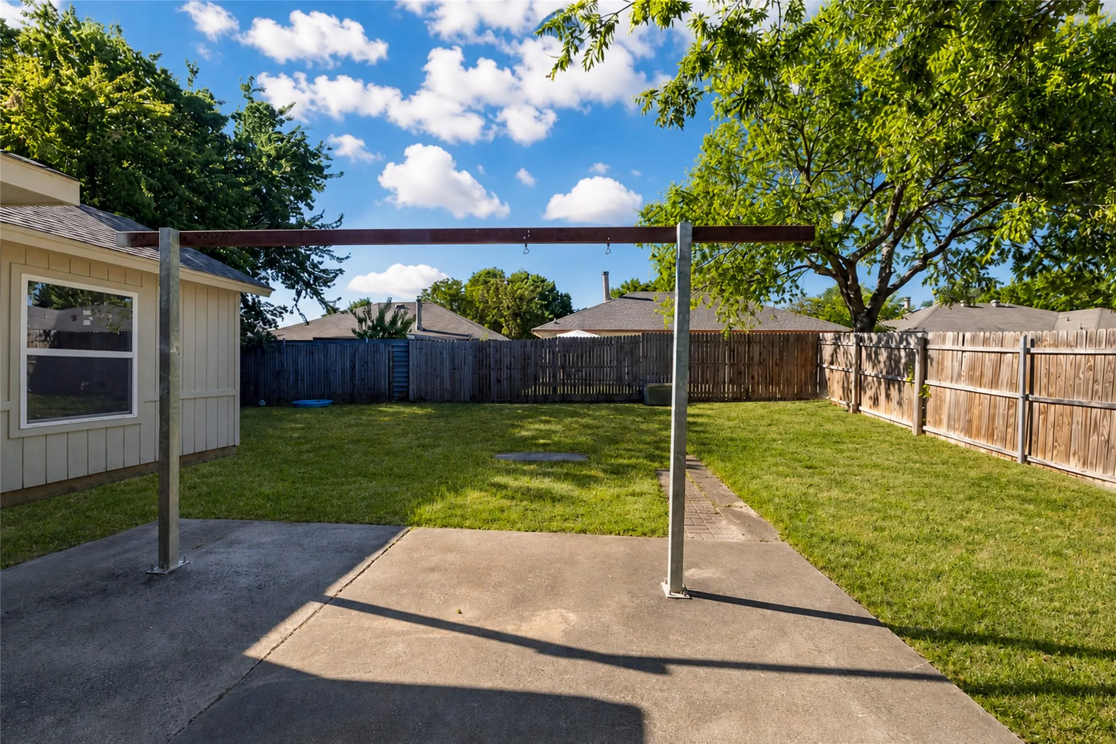 Expansive fenced backyard with a concrete patio, established lawn, and view of mature trees